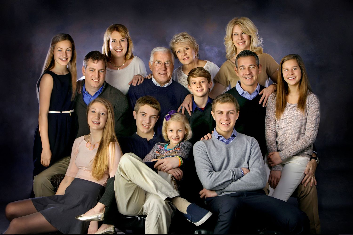 Large family portrait with multiple generations posing together in a professional studio setting with dark background.