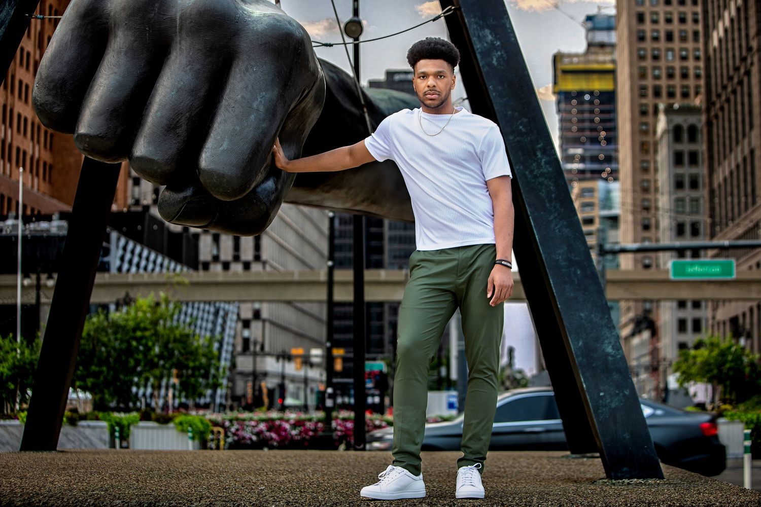 Man in white tee and olive pants poses by Joe Louis Fist sculpture in downtown Detroit.