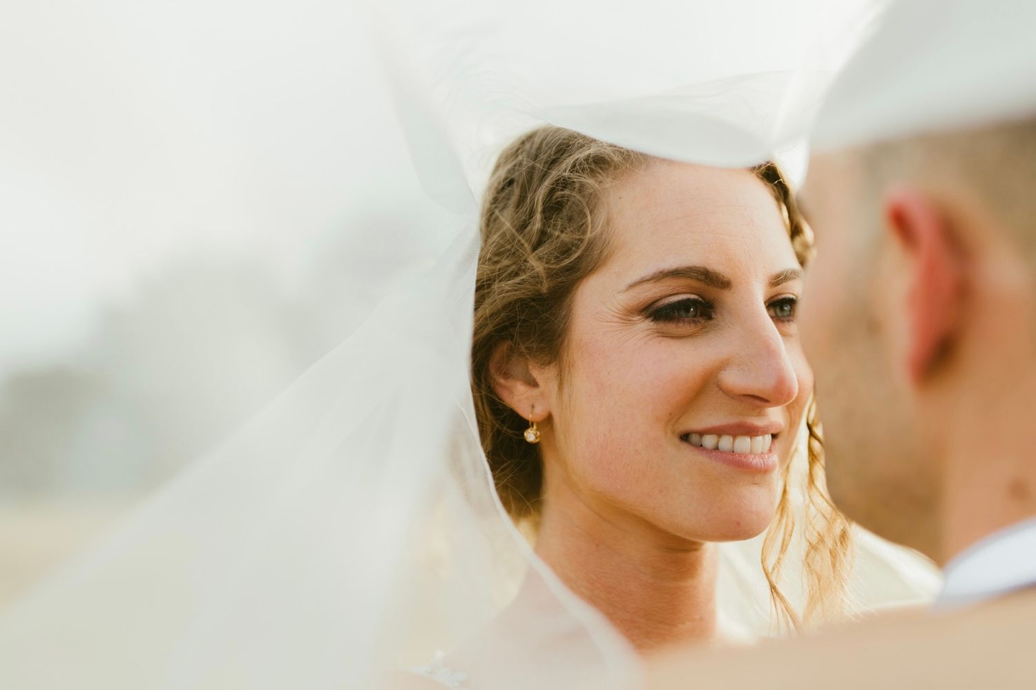 Radiant bride smiling under her veil in a golden hour wedding portrait.