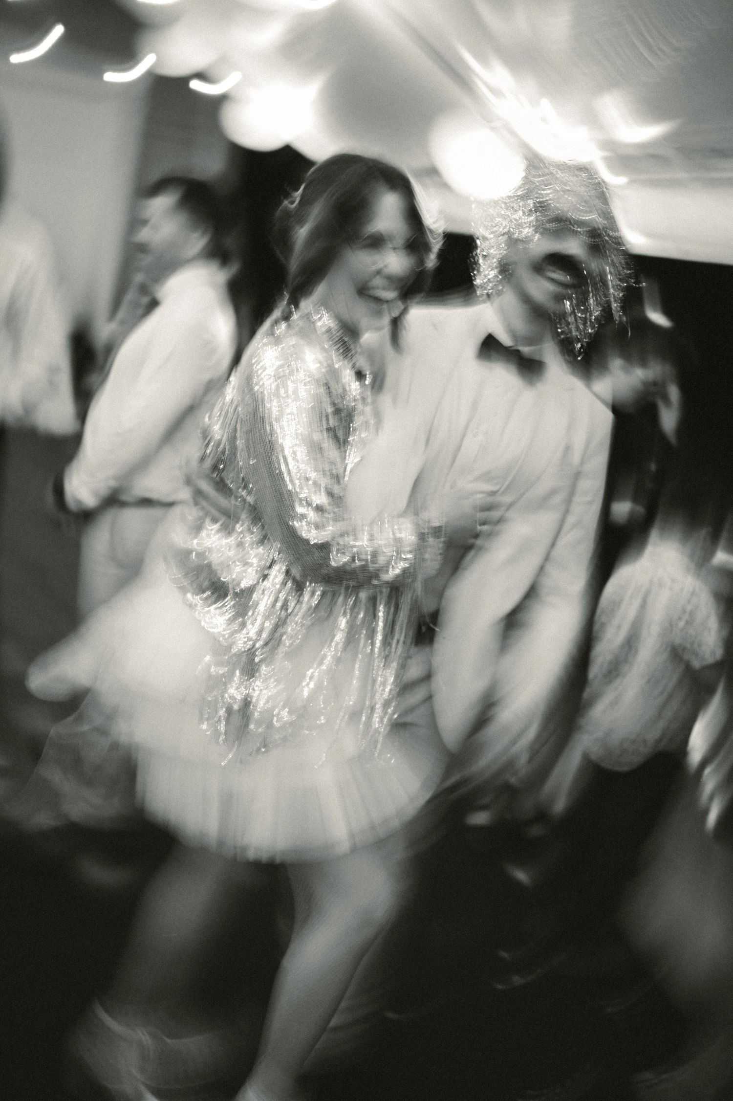 Black and white photo of a woman in a sequin dress dancing joyfully at a formal party event.