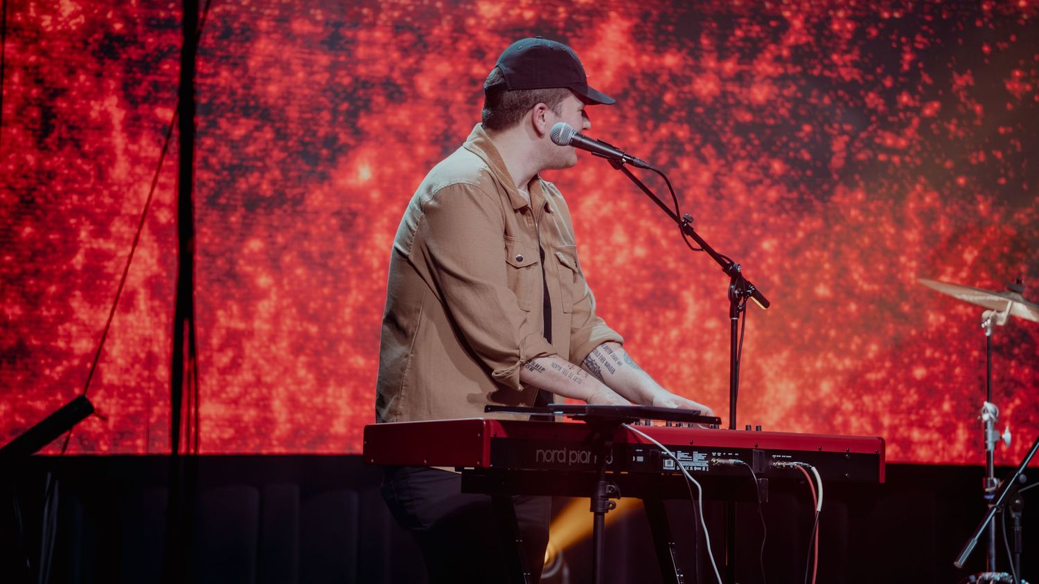 Musicians perform on stage with dramatic red lighting and smoke effects during a live concert performance.