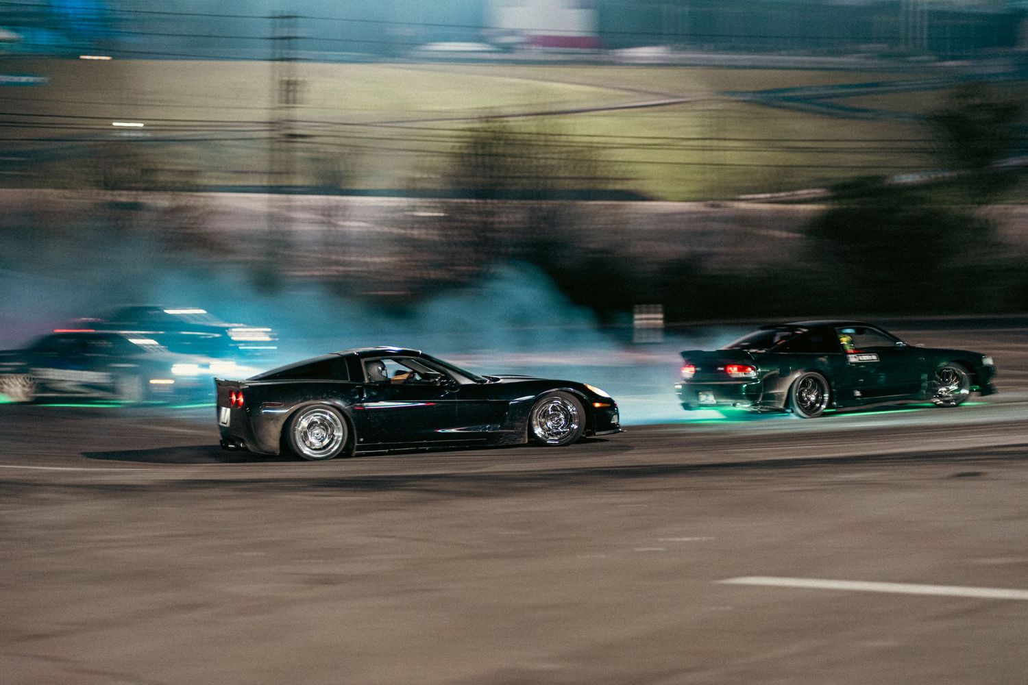 Two racing cars drifting side by side on a racetrack during a drift show event.
