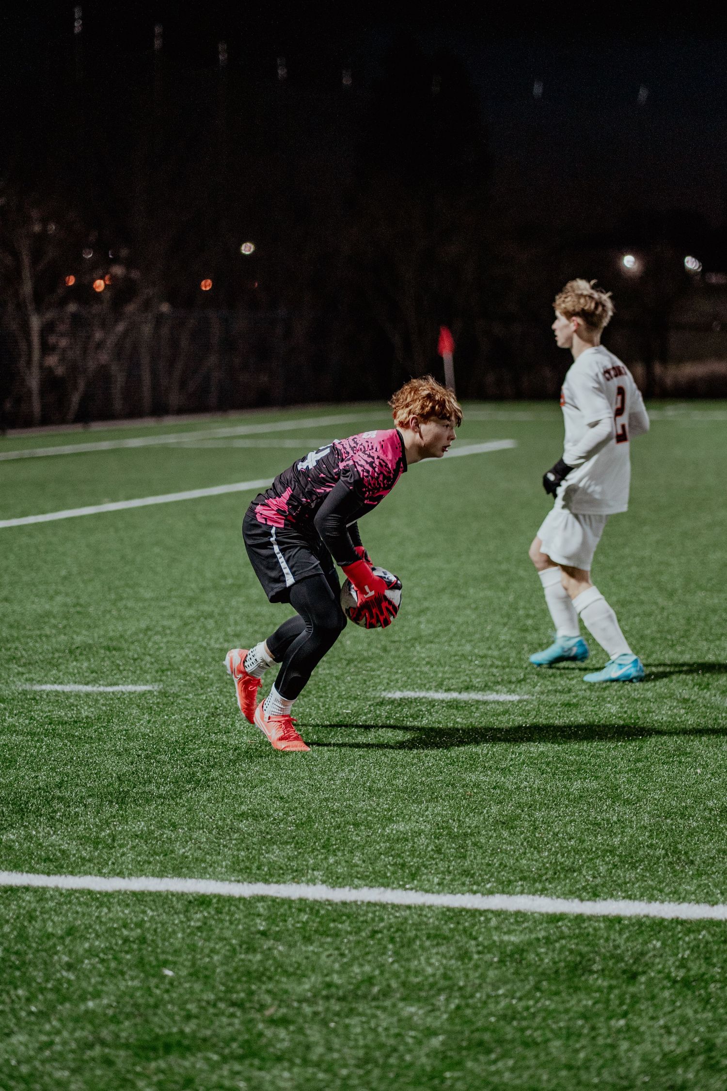 Two young soccer players practice on an illuminated artificial turf field at night during a training session.
