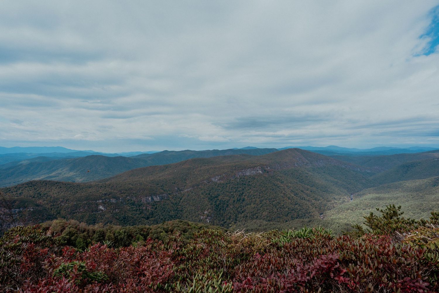 A panoramic mountain vista showcases rolling peaks and valleys under cloudy skies in autumn colors.