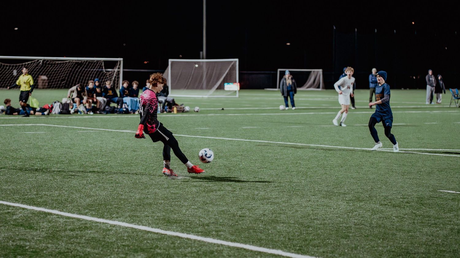 A soccer match takes place on an illuminated artificial turf field at night with players in action.