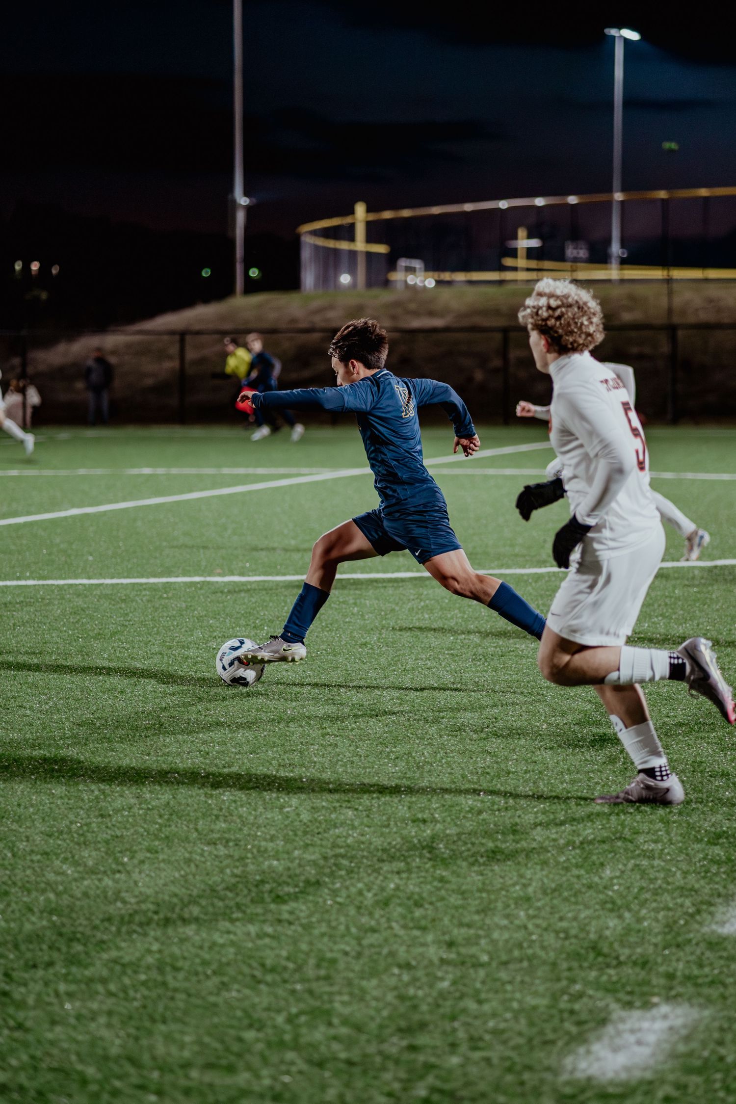 Soccer players compete intensely on an illuminated turf field at night during a competitive match.