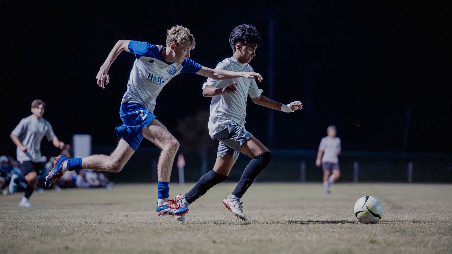 Soccer players in blue and white uniforms compete for possession of the ball during a match.