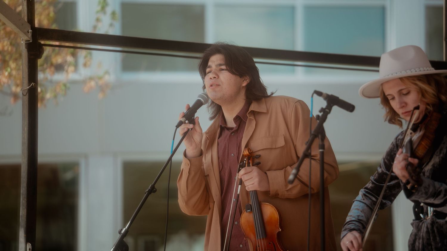 Musicians perform together in warm lighting at an outdoor venue with microphone stands and musical equipment.