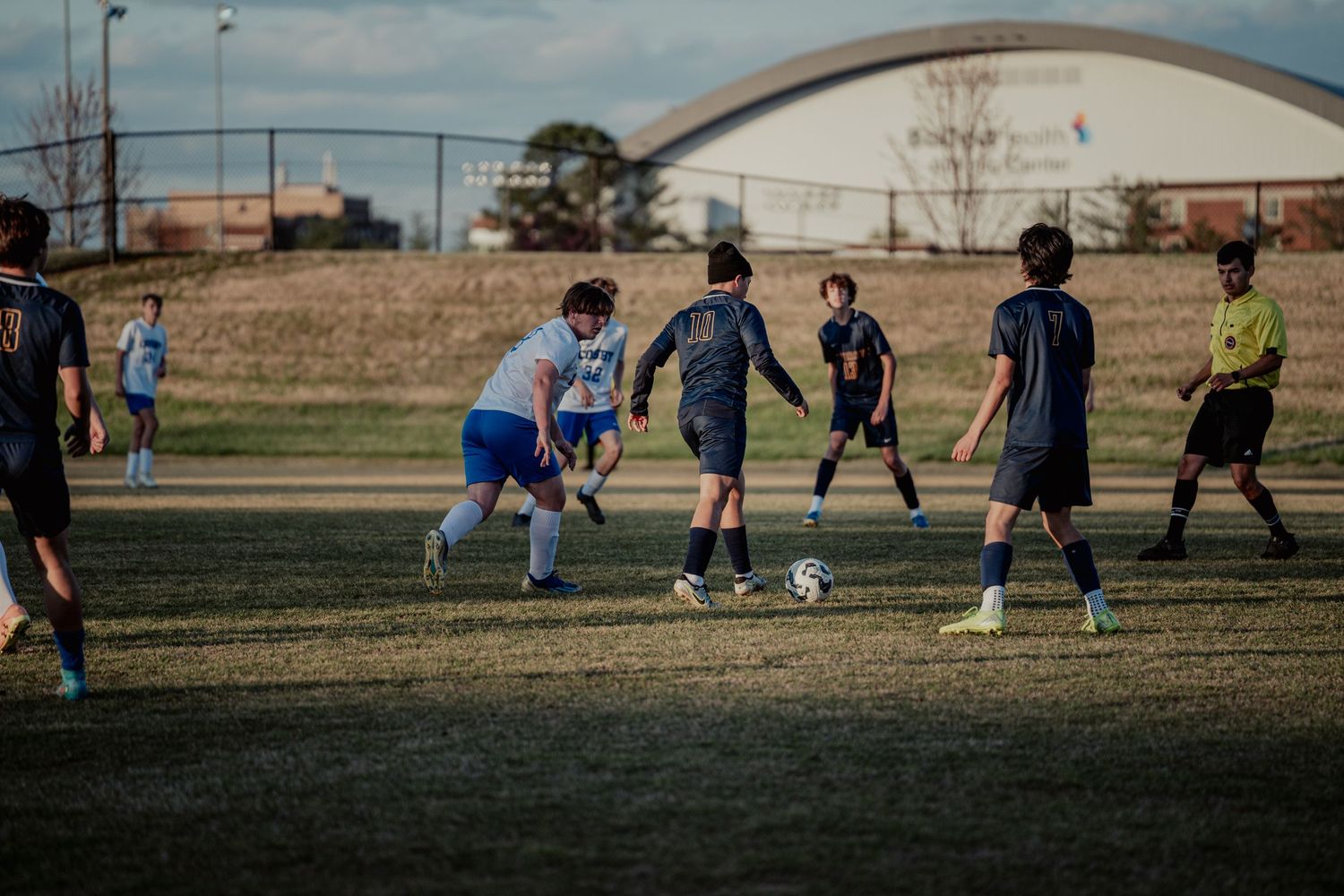 Soccer players compete on a field during a recreational match in the late afternoon golden sunlight.