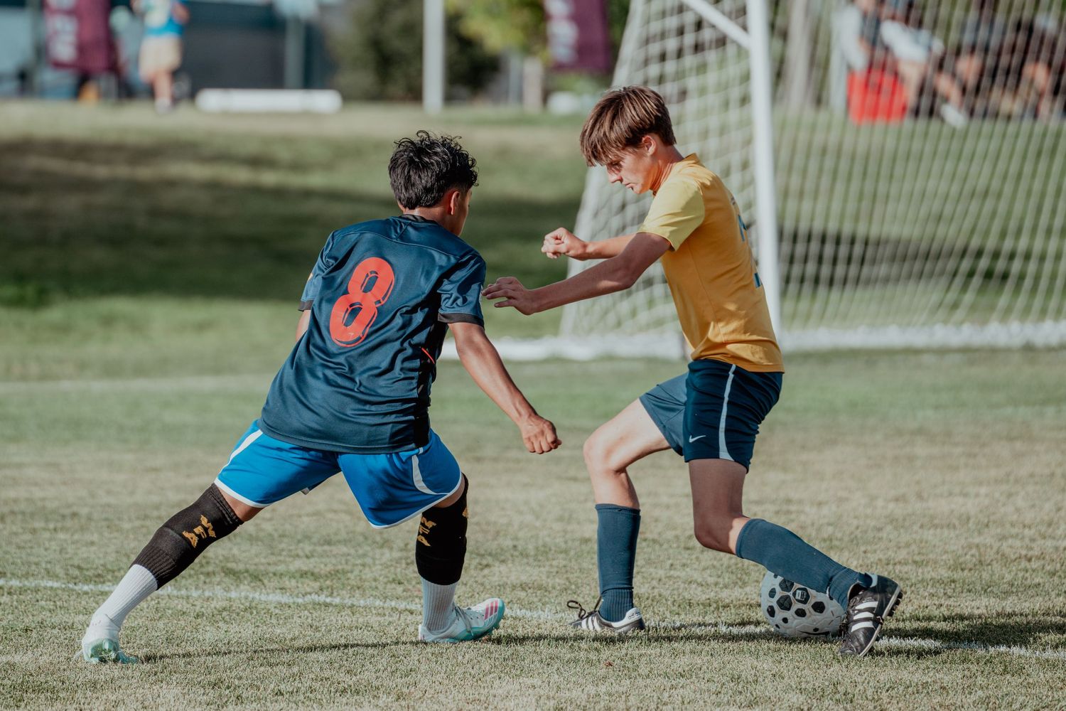 Two youth soccer players compete for the ball during a match on a green grass field.