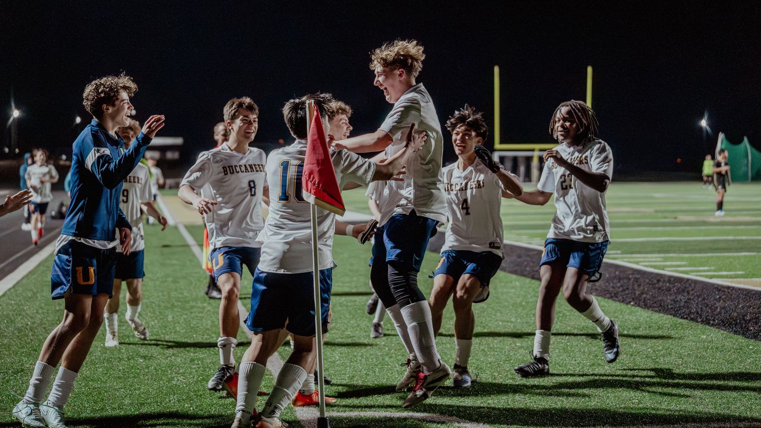 Athletes celebrate on a turf field during a nighttime sports game under bright stadium lights.