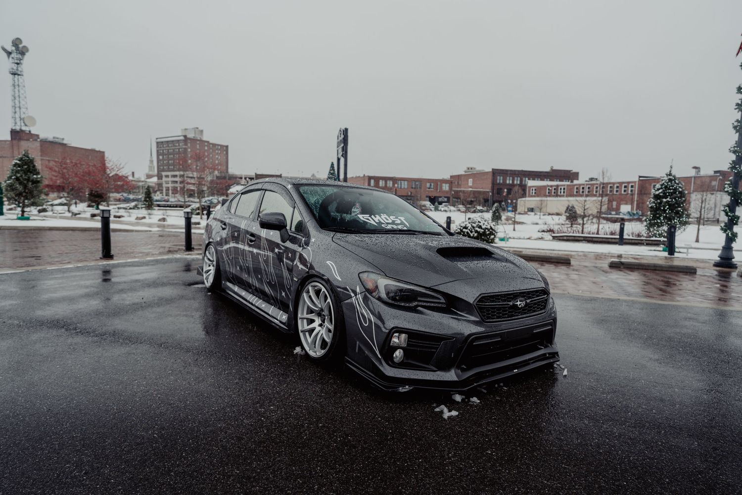 A gray Subaru WRX STI sports car parked in a wet parking lot on an overcast winter day.