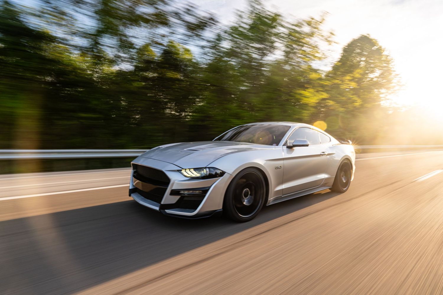 Silver Ford Mustang driving on a road during golden hour sunset with motion blur effect.