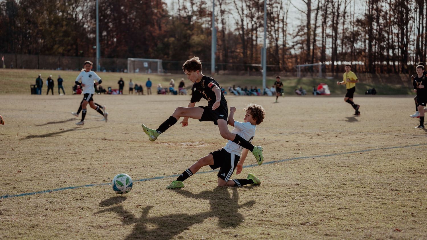 Soccer players compete for the ball on a dry grass field during a match on a sunny day.