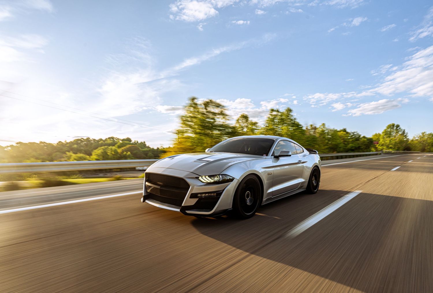 Silver Ford Mustang speeding on highway during sunset with motion blur effect.