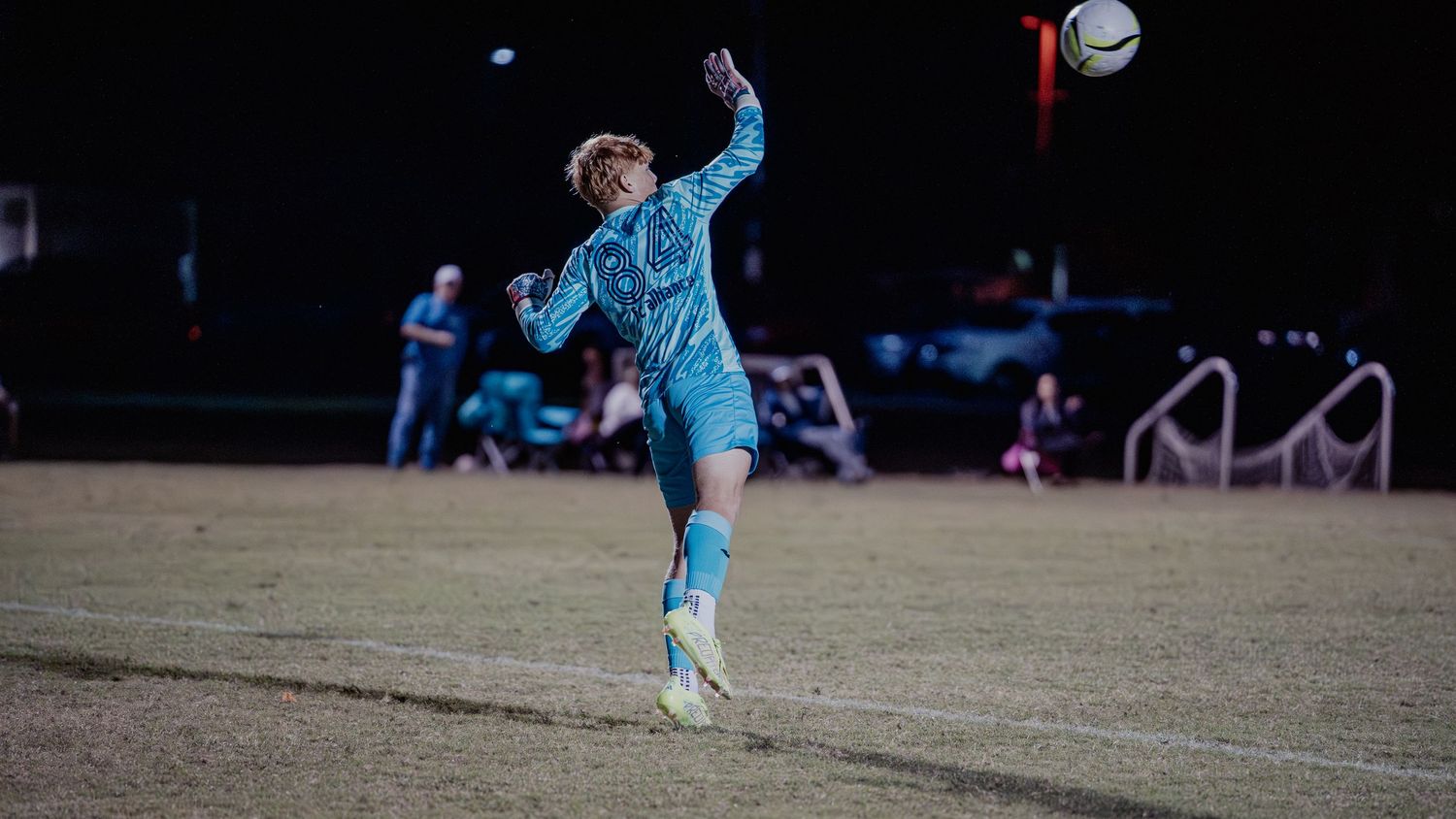 A soccer player in blue uniform performs a diving save to block the ball during a match.