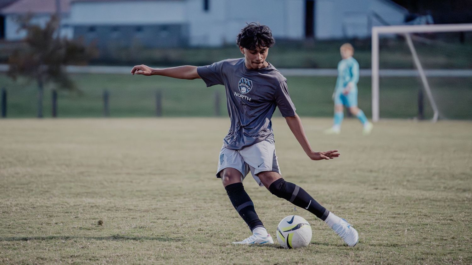 Soccer player in gray uniform dribbles ball across grass field during competitive match.