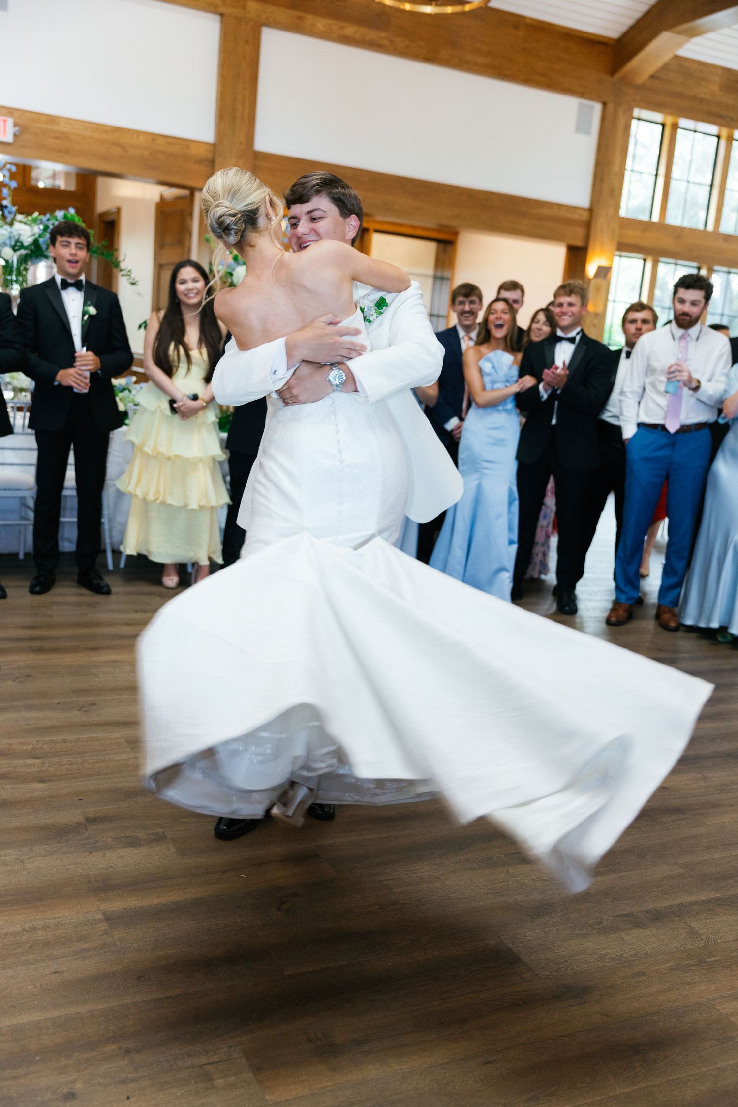 Bride and groom perform a joyful spinning dance move on wooden floor during their wedding reception.