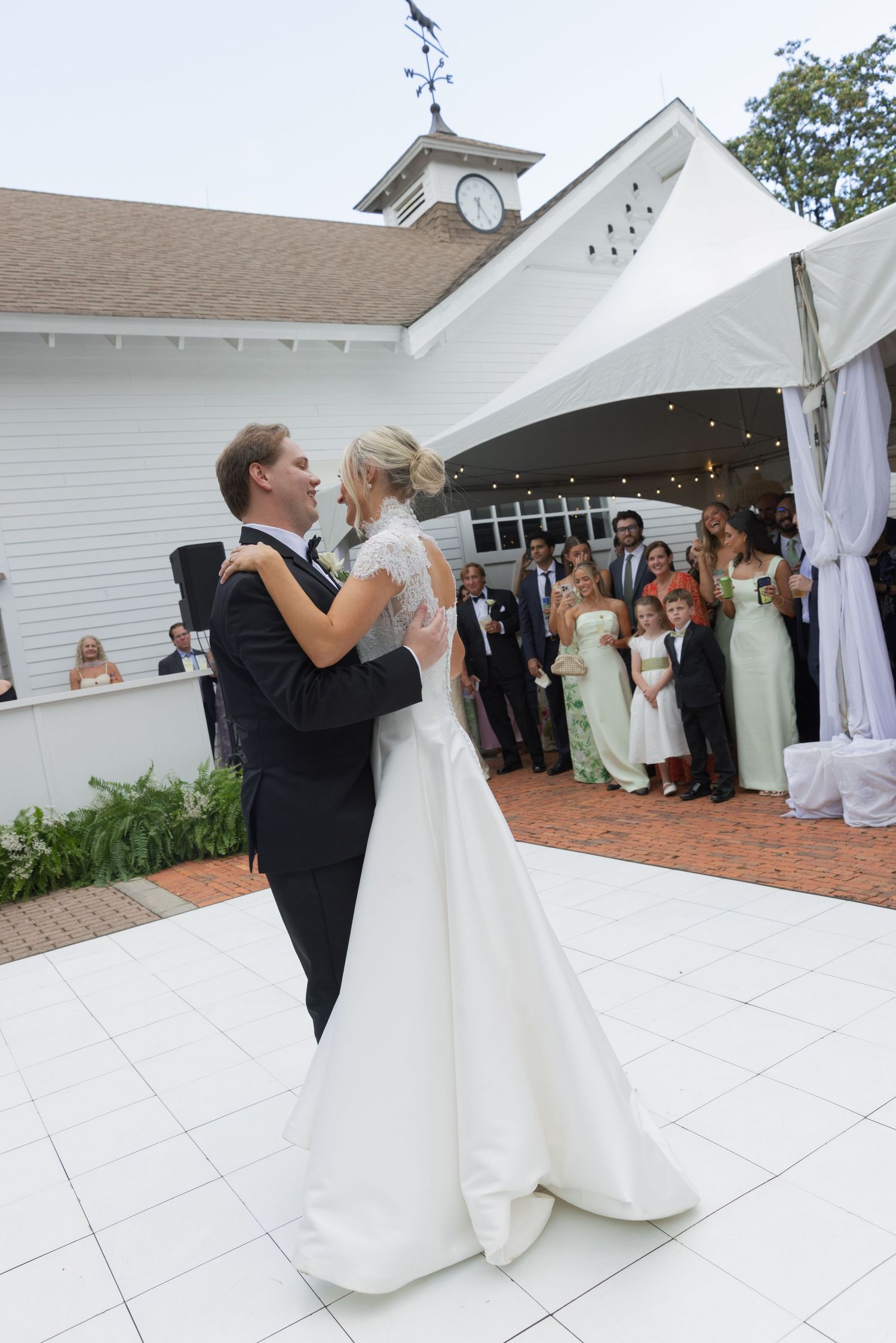 Bride and groom share their first dance on white outdoor dance floor while wedding party watches at Southern venue.