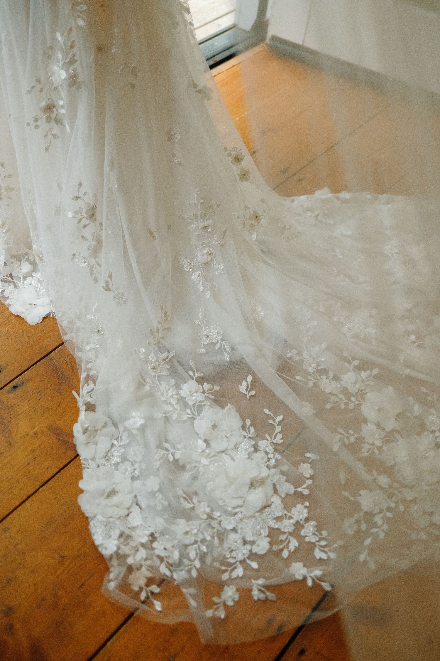 Close-up details of delicate white lace and beading on a wedding dress against wooden flooring.