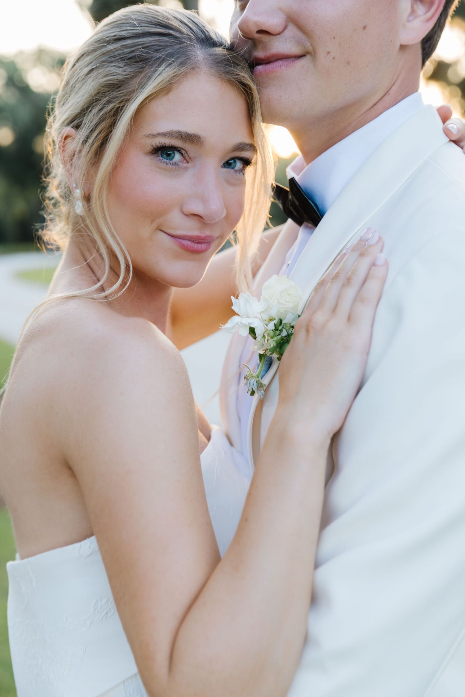 A romantic wedding portrait of a couple in formal attire embracing outdoors during golden hour.