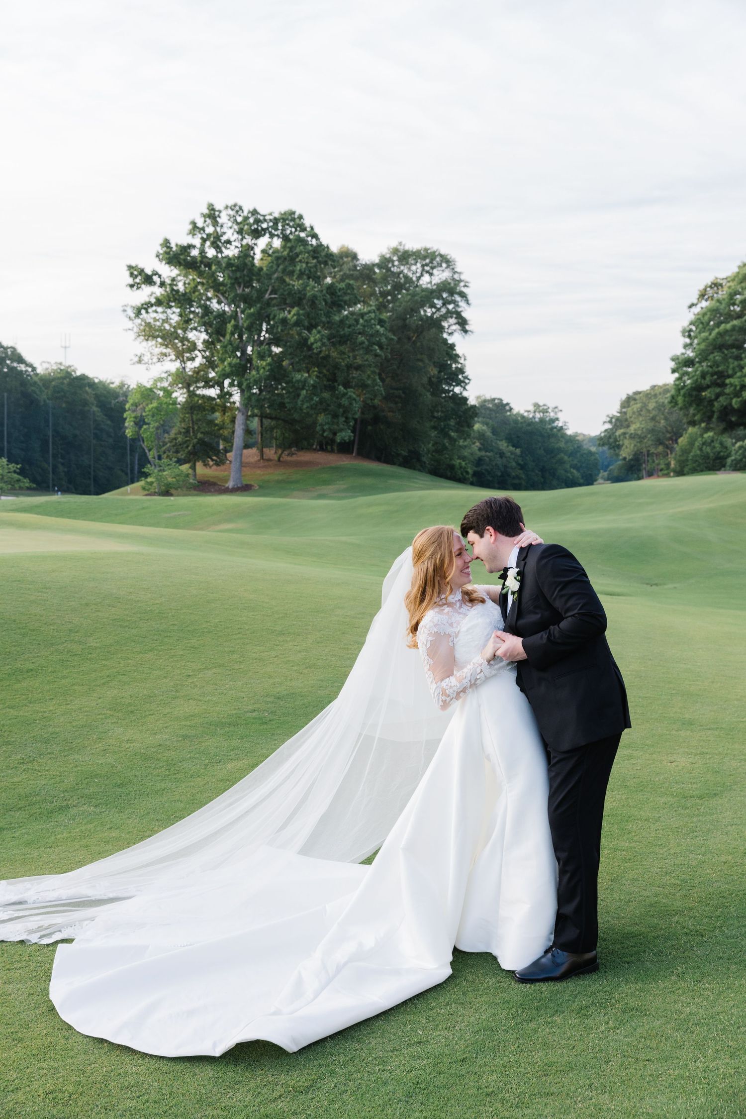 A couple shares their first kiss as newlyweds on a lush green golf course with a flowing white wedding dress.