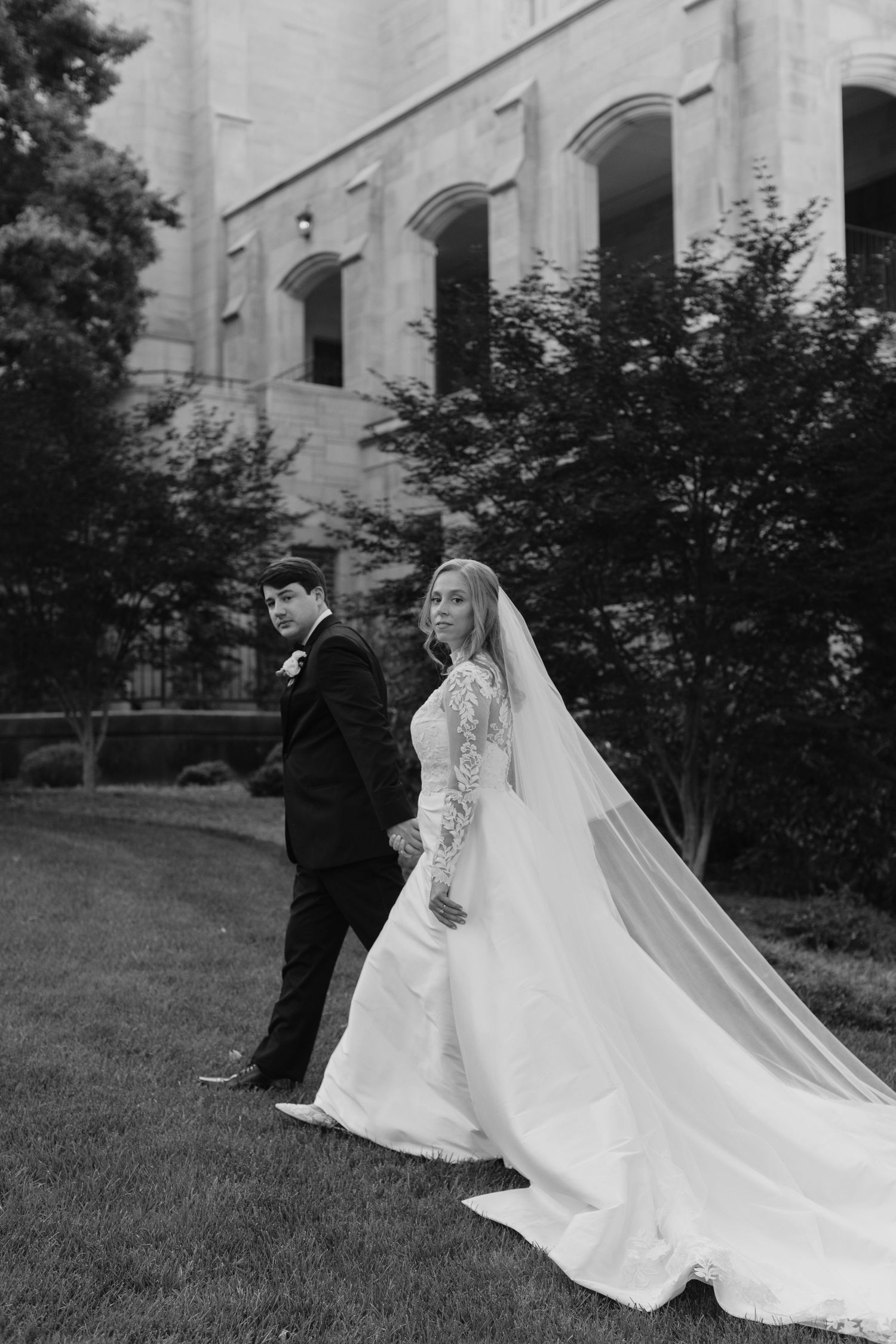 A romantic black and white wedding photo series showing a couple in formal attire on a grassy lawn by a building.