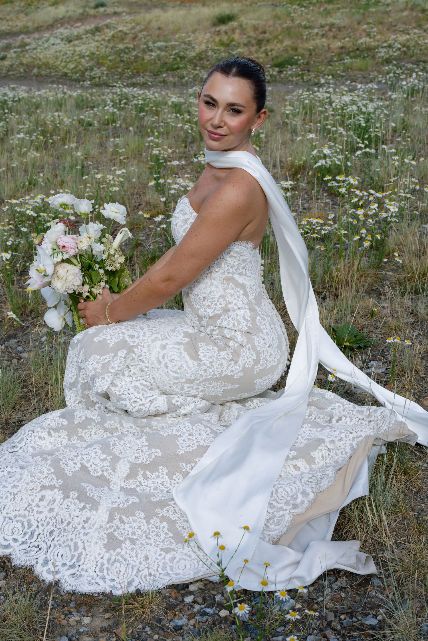 Wedding dress with intricate lace detailing laid out in a meadow with wildflowers.