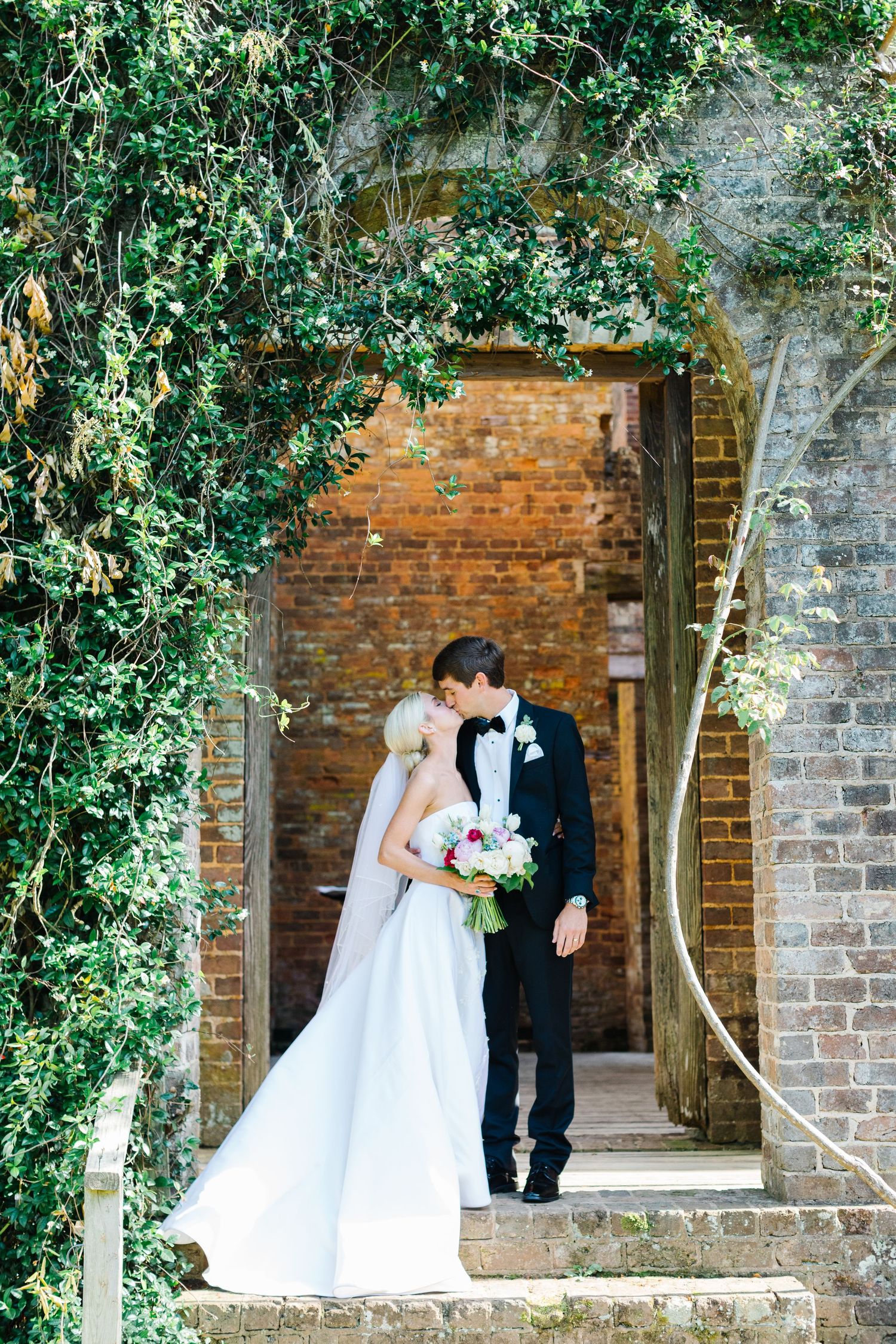 A romantic wedding moment captured in a series of photos against a rustic brick wall with lush greenery.
