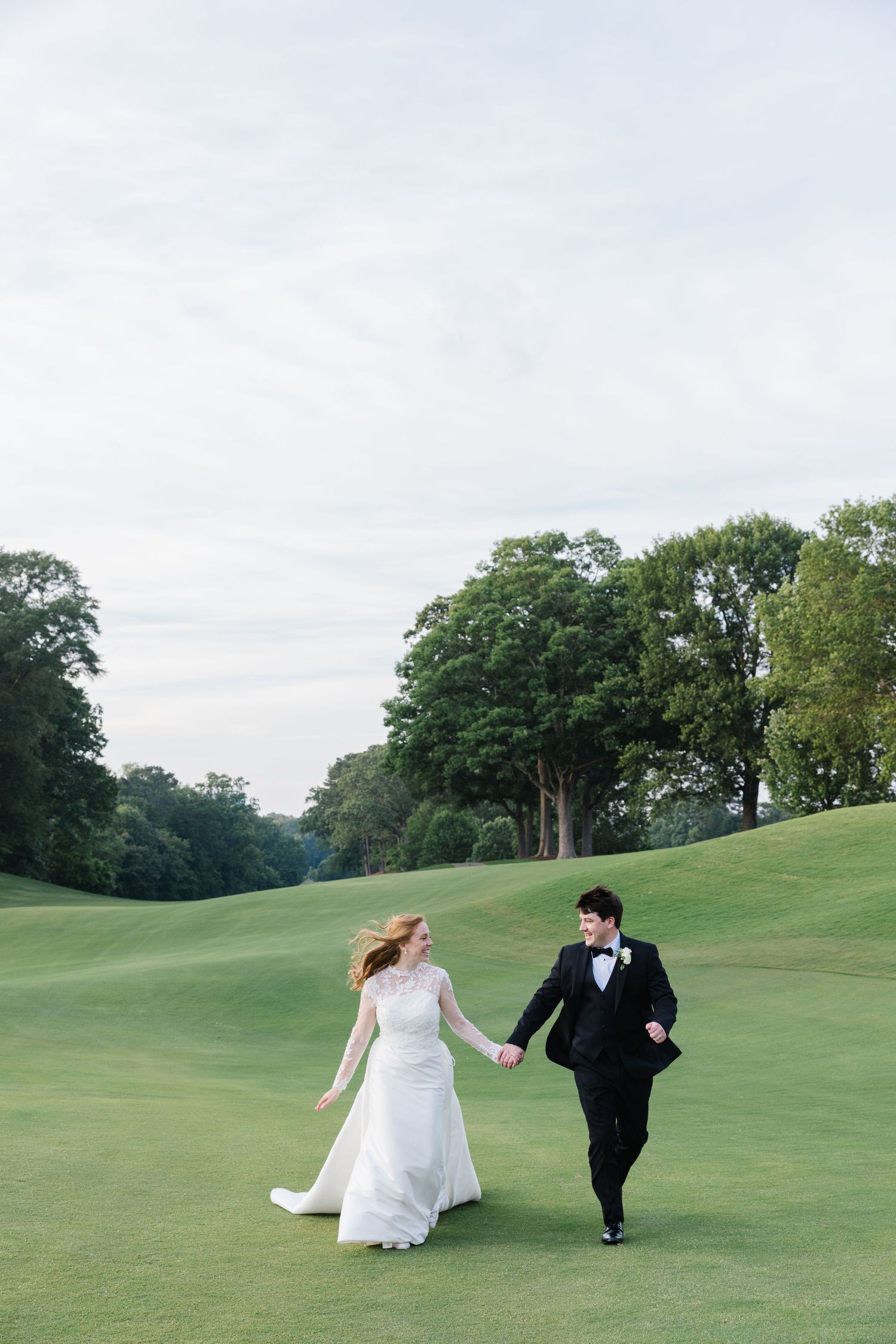 Newlyweds run hand in hand across rolling green golf course hills.