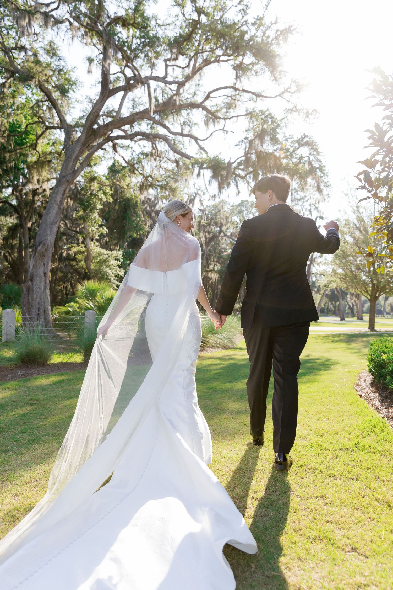A couple shares a romantic moment in an outdoor garden setting as sunlight filters through Spanish moss-draped trees.