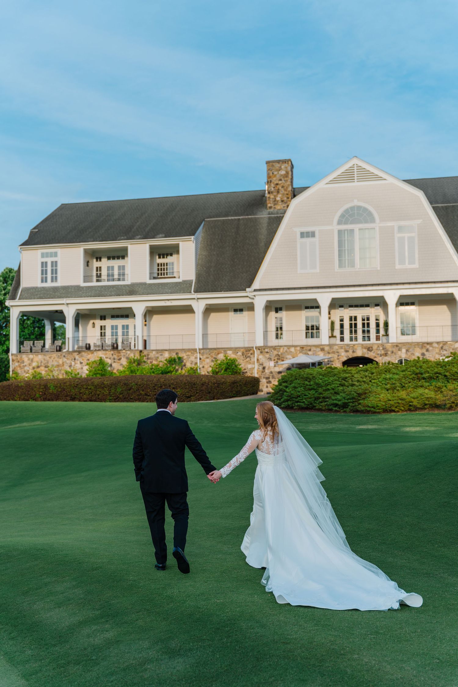 Couple walks towards elegant stone clubhouse on manicured golf course grounds.