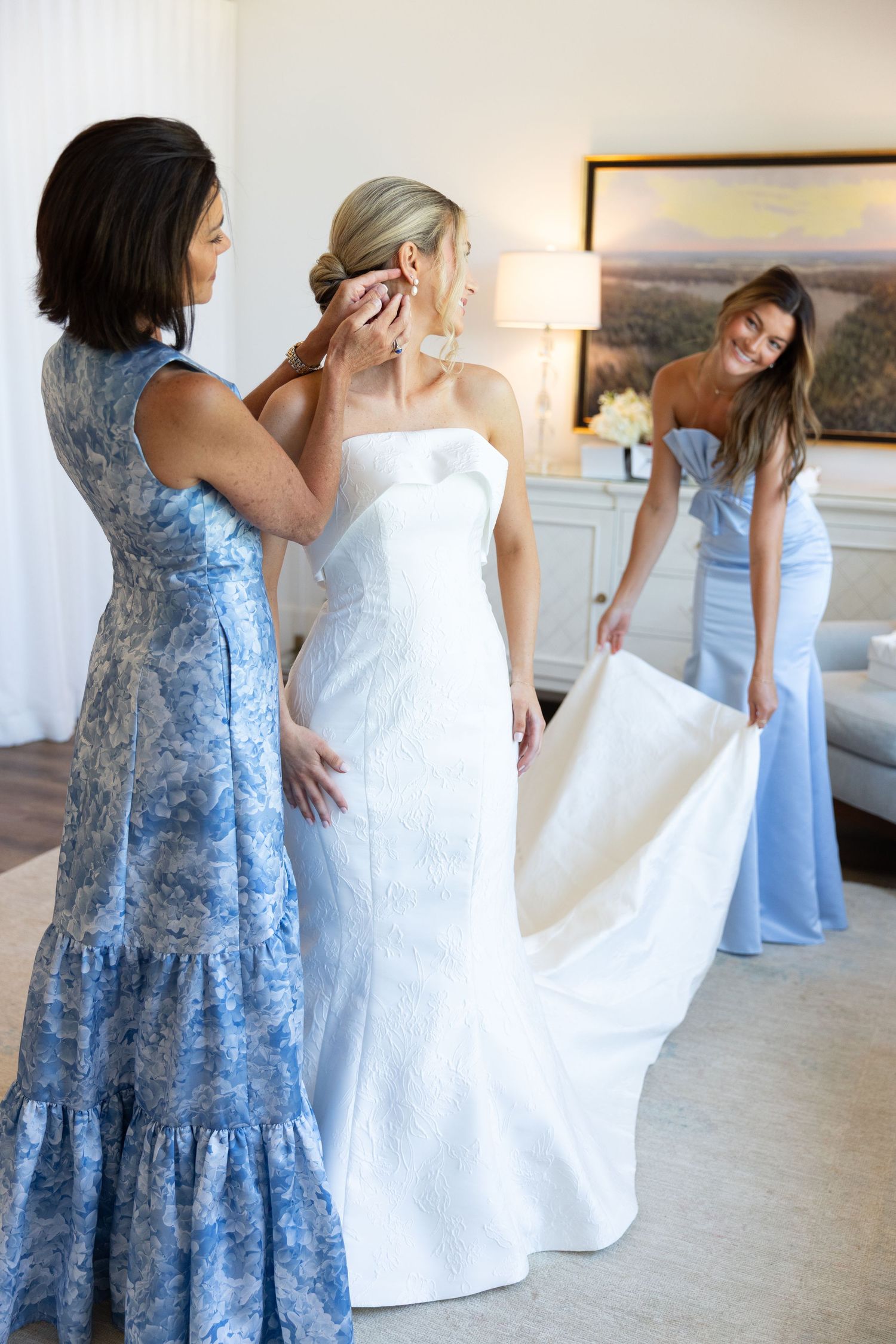 Wedding preparation scene showing a white bridal gown and person in blue floral dress helping with arrangements.