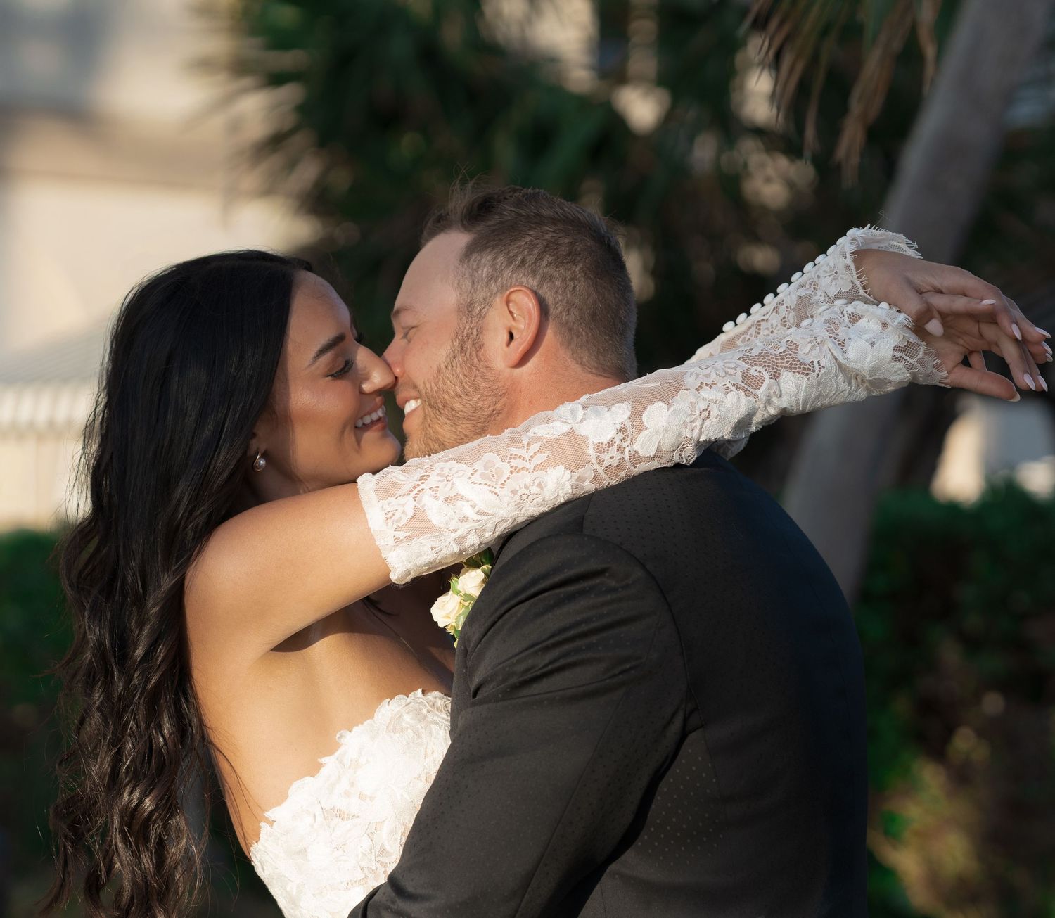 A bride and groom share a romantic kiss outdoors, with the bride wearing a lace wedding gown and the groom in a suit.