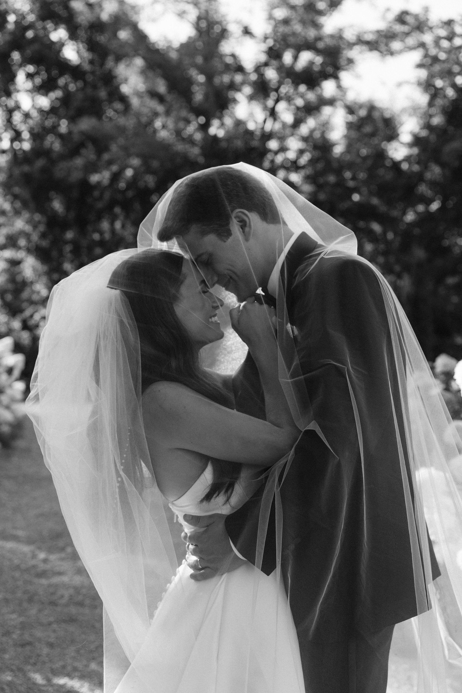 A romantic black and white wedding photo shows a tender moment between newlyweds as the bride's veil flows in the breeze.