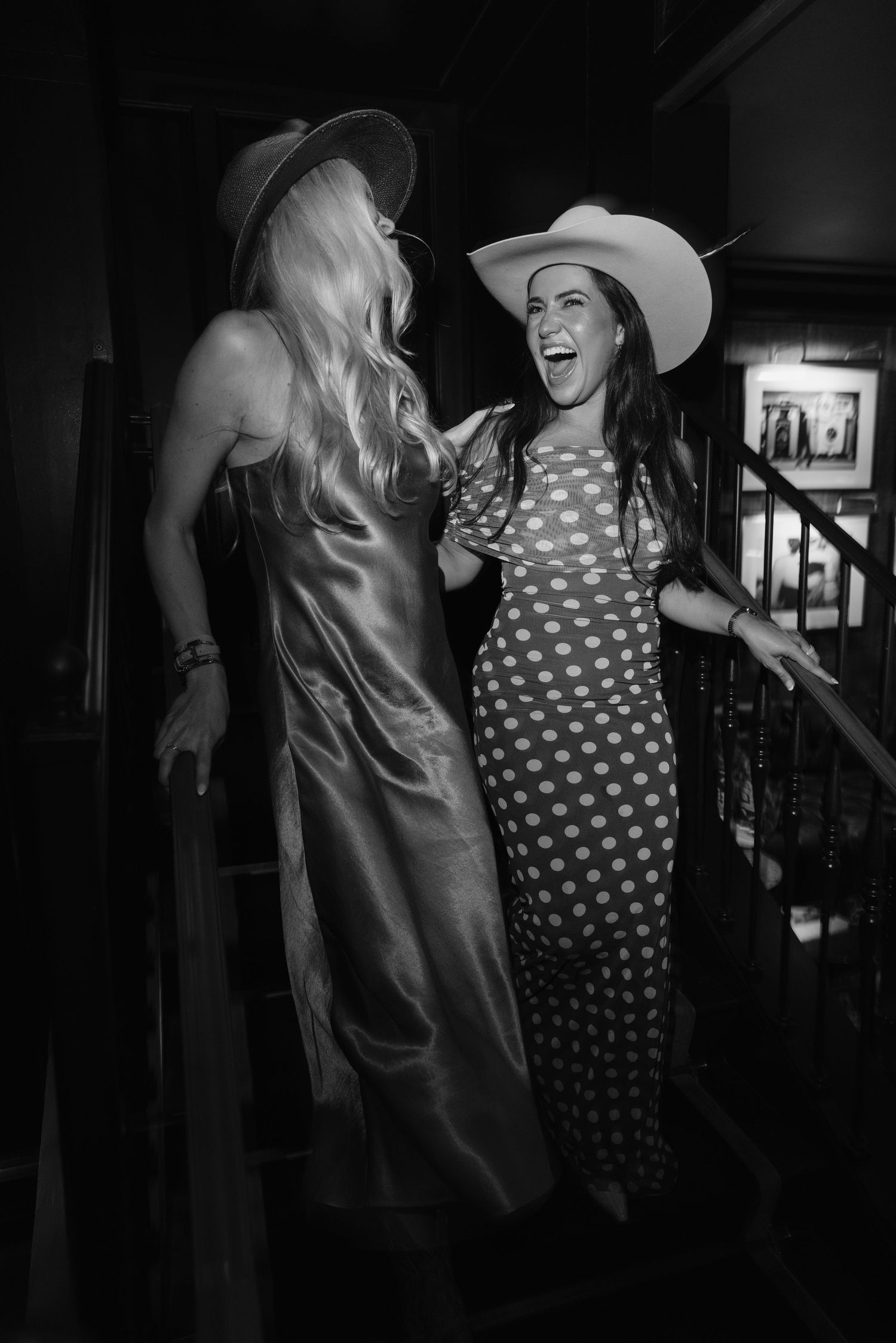 Two people in black and white laughing and dancing together at a party, one wearing polka dots and one in a solid dress.