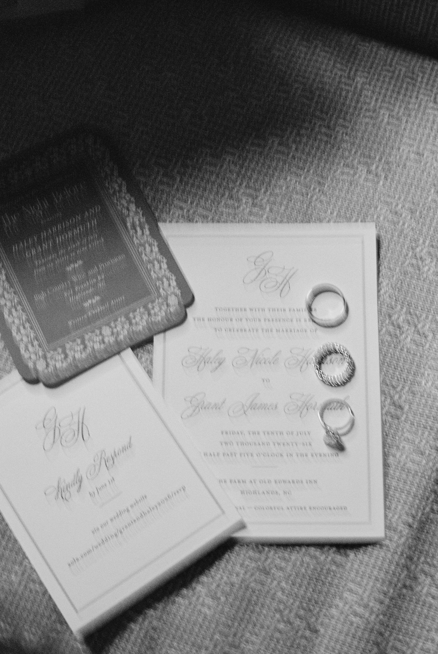 Black and white photo of an elegant monogrammed wedding invitation suite with three wedding rings resting on the card.