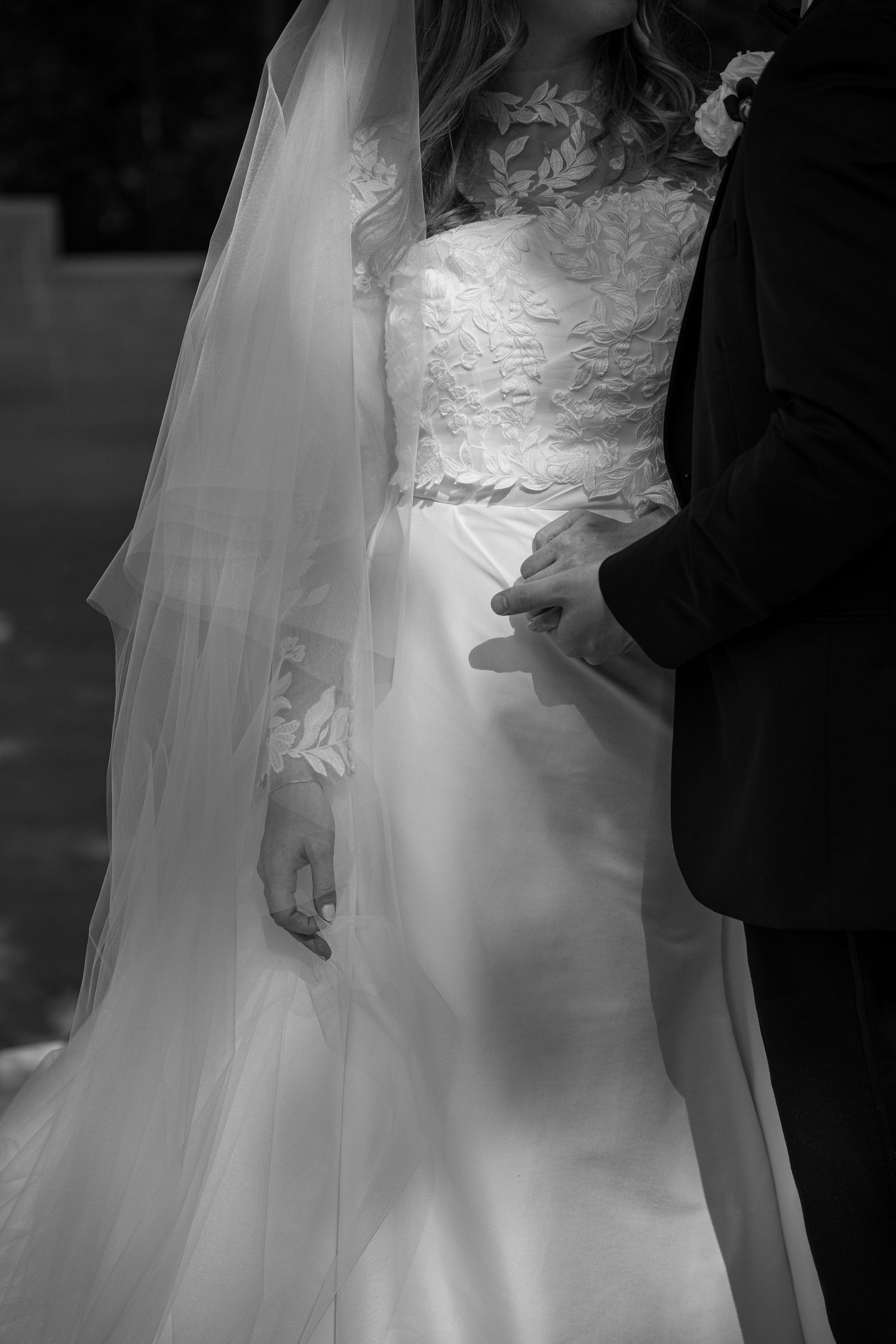 Close-up details of a bride's white wedding dress with delicate lace patterns and flowing fabric.