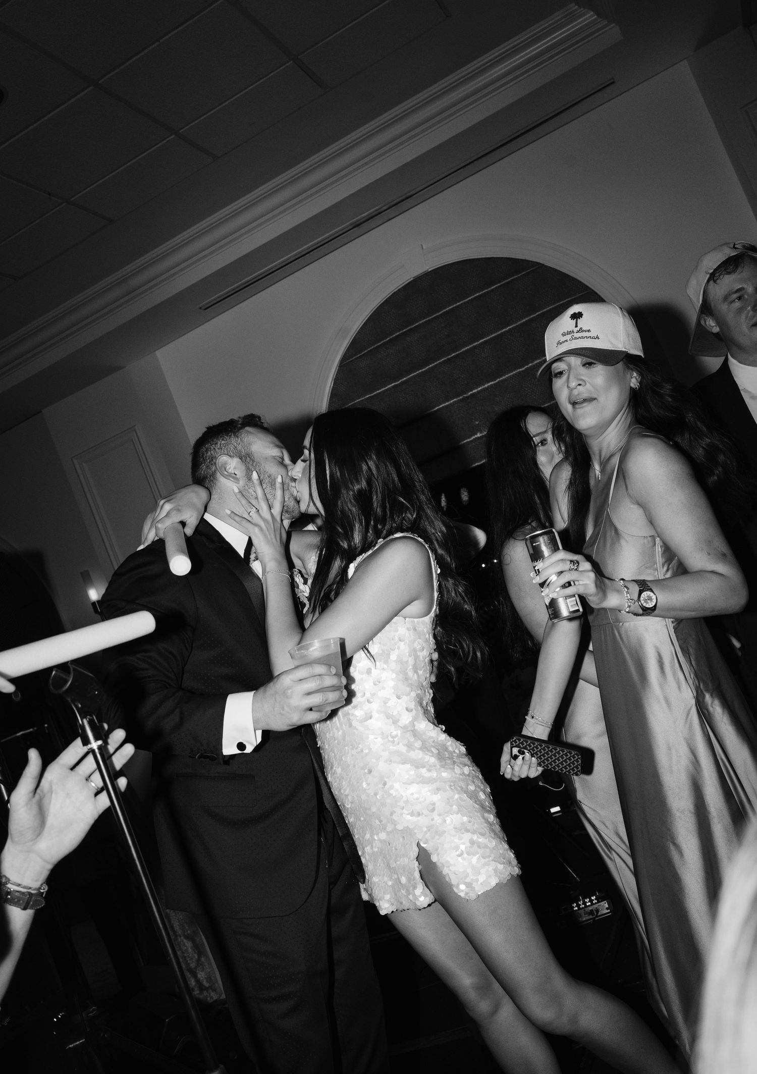 Couple sharing a kiss at a lively wedding reception party in black and white photography.