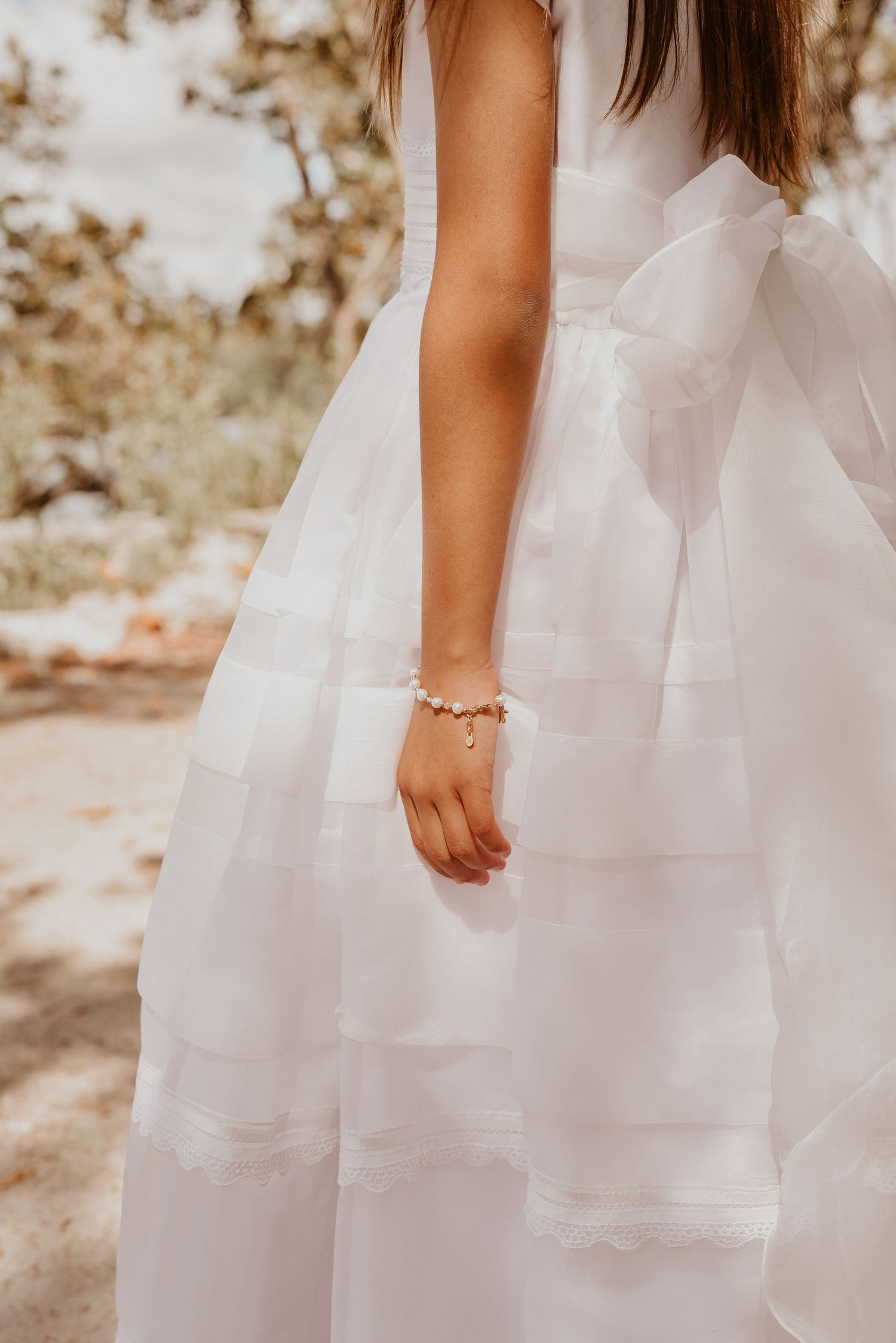 Child in white dress by beach holding rosary during First Communion portrait session