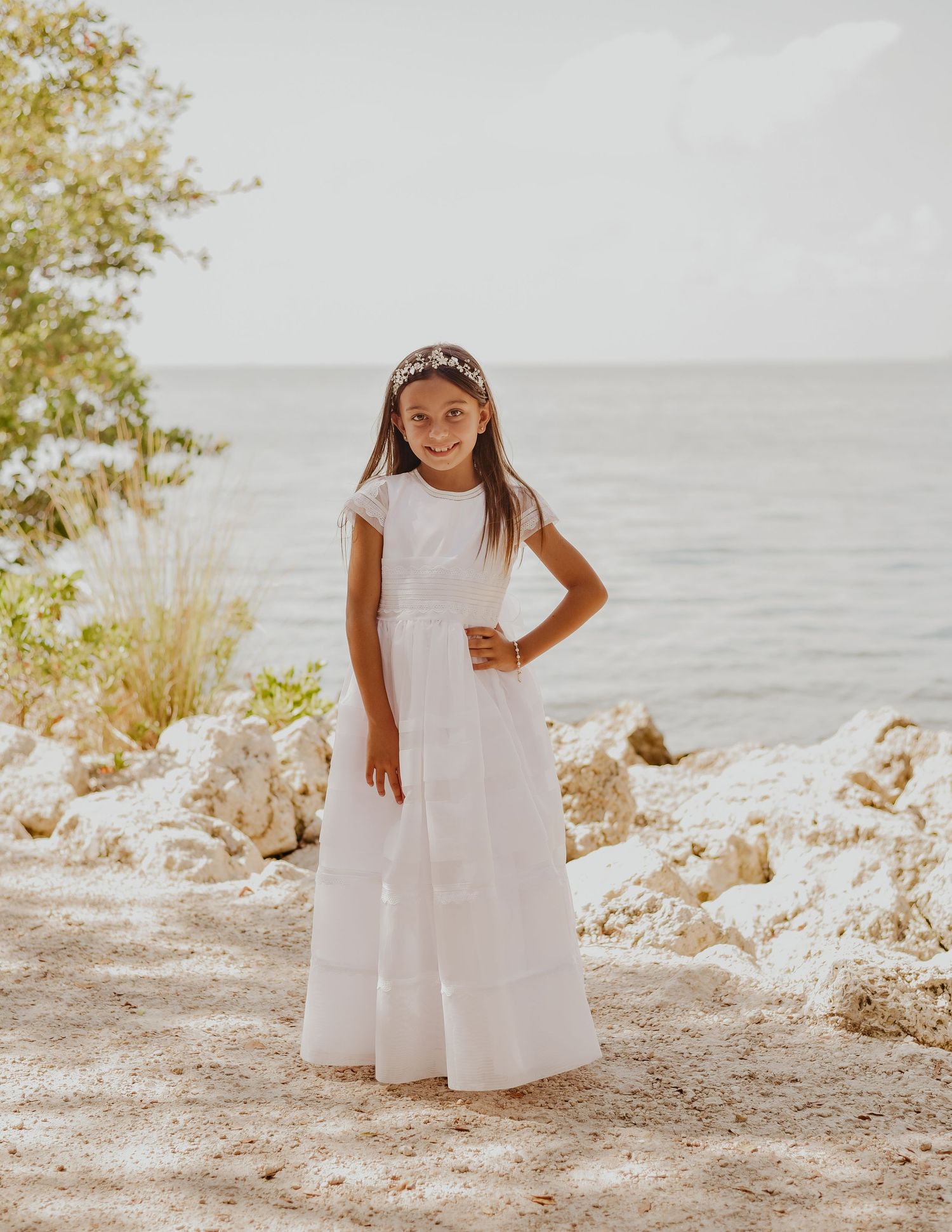 Child in white dress by beach holding rosary during First Communion portrait session
