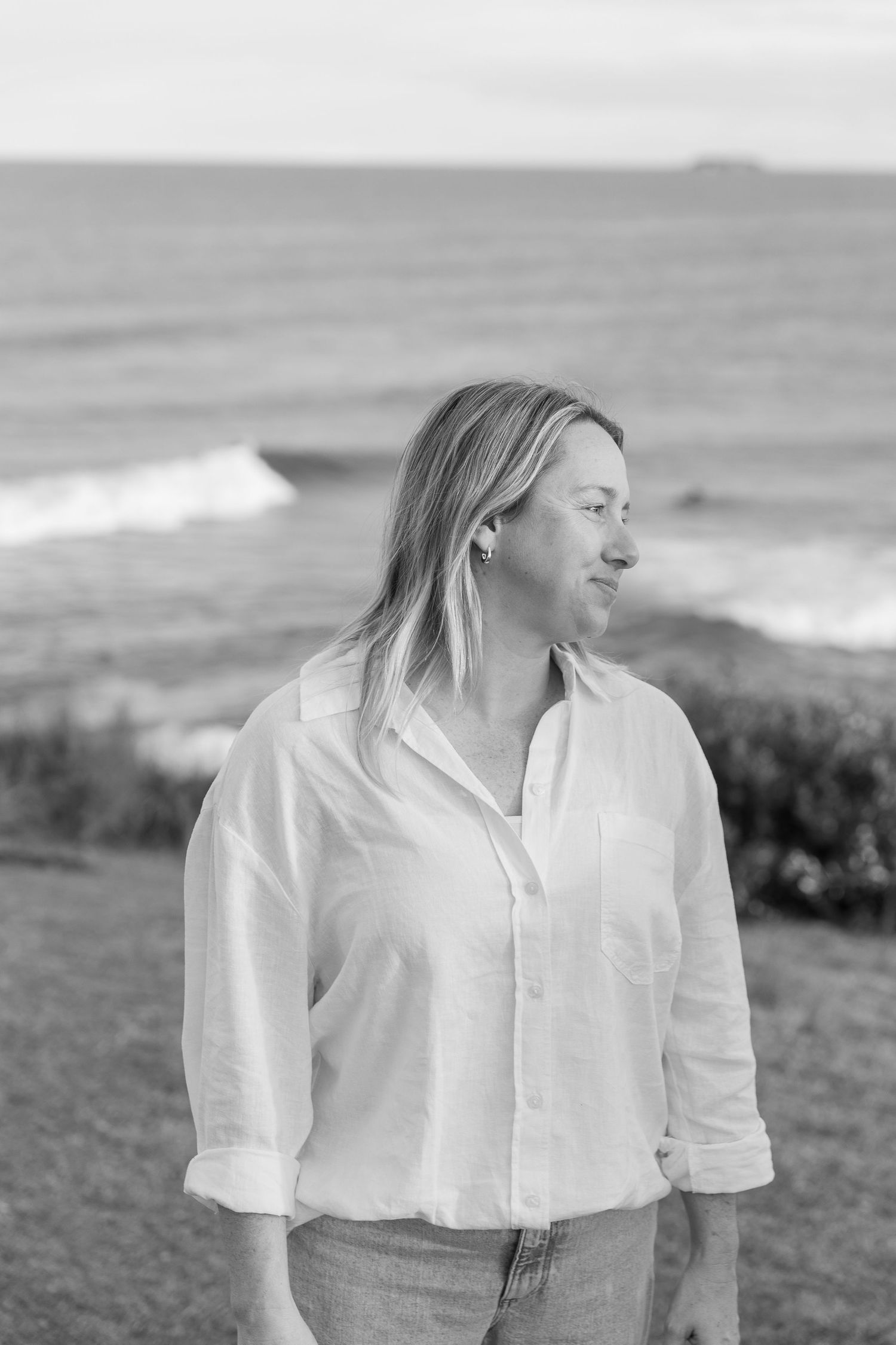 Black and white portrait of someone in a white shirt against a coastal landscape.