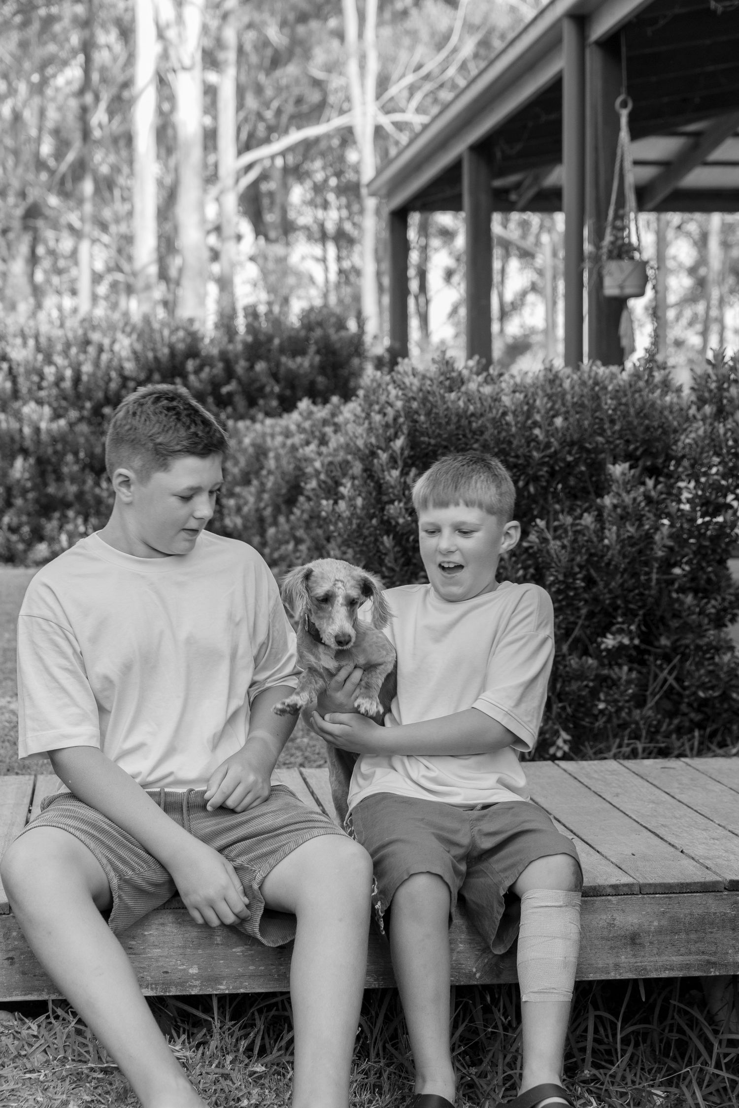 Two children sit together on a wooden deck sharing a playful moment in black and white.