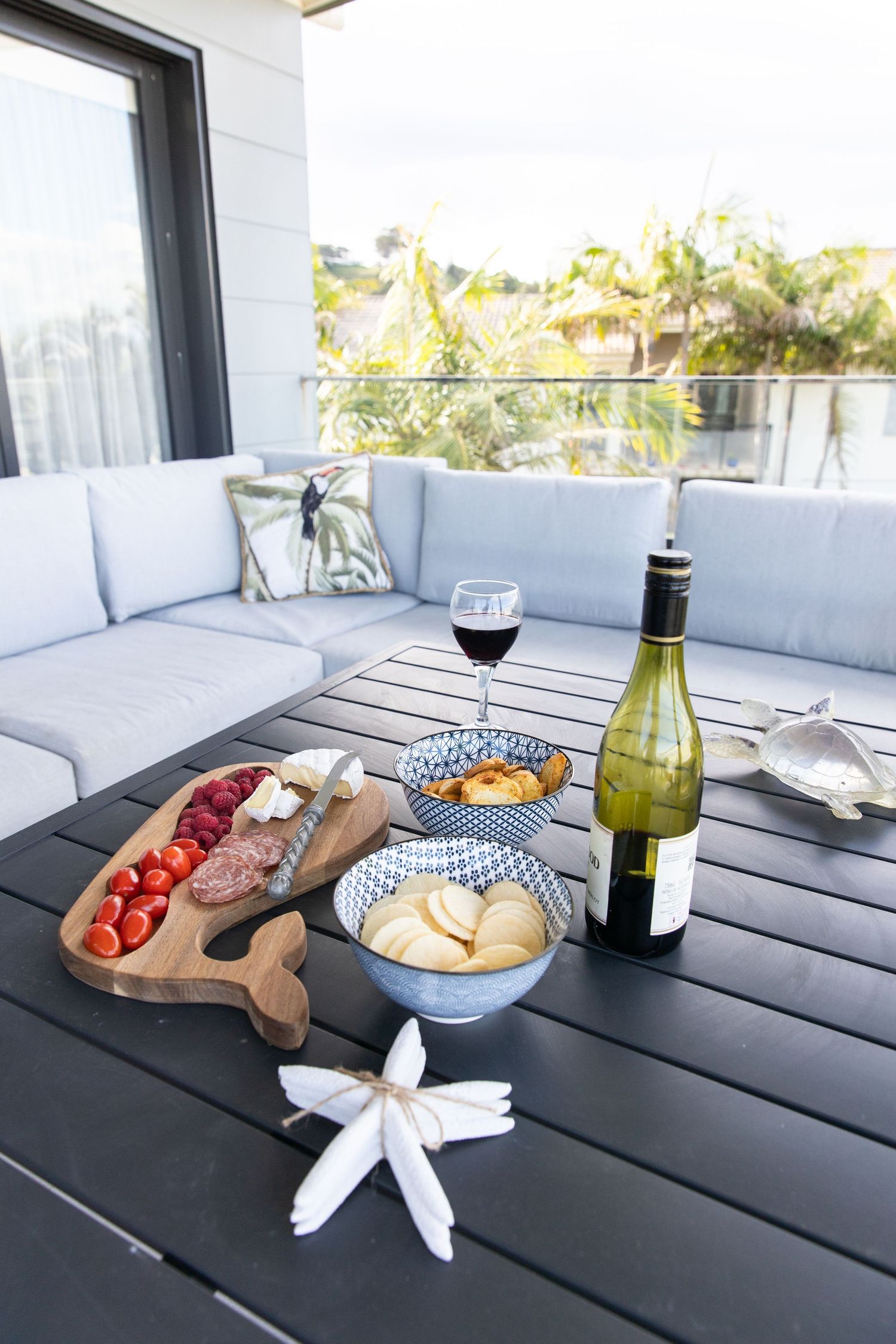 Outdoor dining setup with wine, cheese board and appetizers on a modern patio table.
