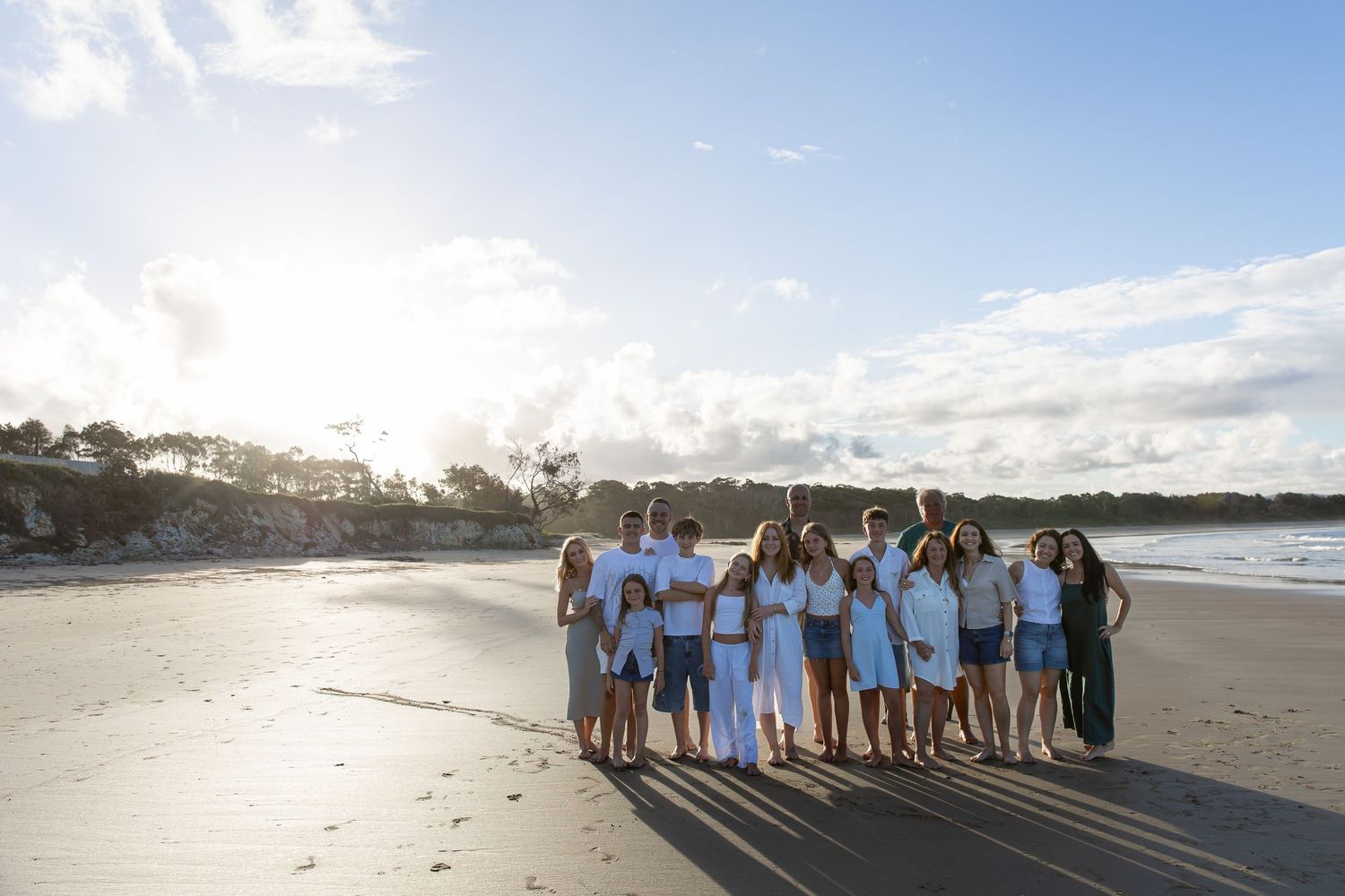 Large family group posing together on a sunny beach, dressed in white and light blue outfits in Mullaway, Coffs Harbour.