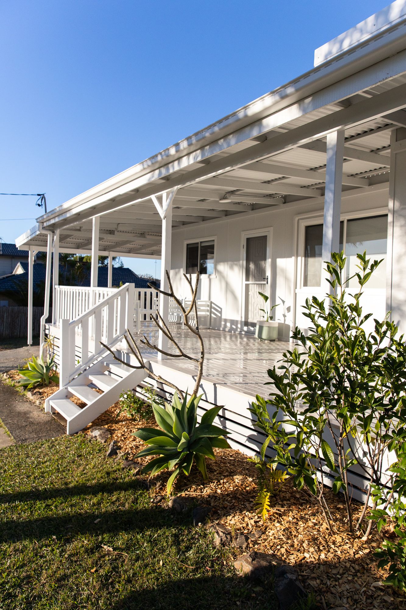 Modern white porch with tropical landscaping and stone garden features along the exterior.