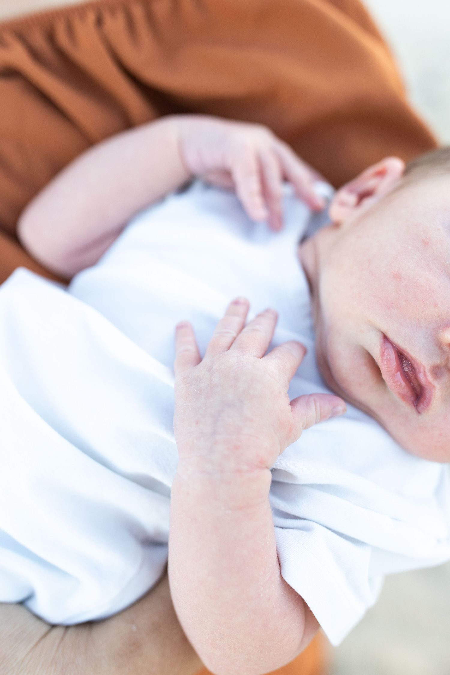 Close-up of a newborn baby with mild skin rash lying on a caregiver, wearing a white onesie.
