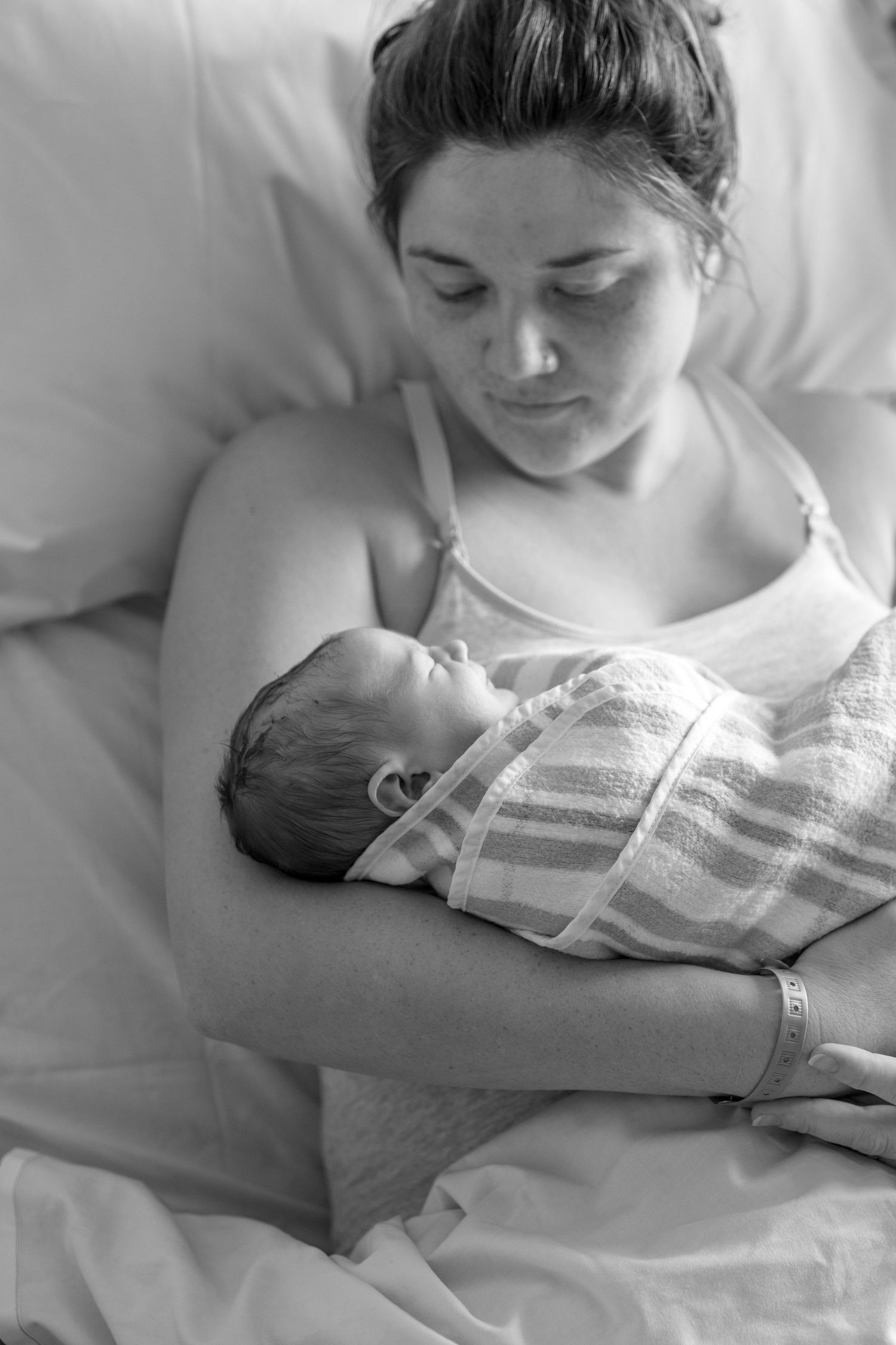 Black and white photo of a new mother in hospital bed tenderly gazing at her swaddled newborn baby.