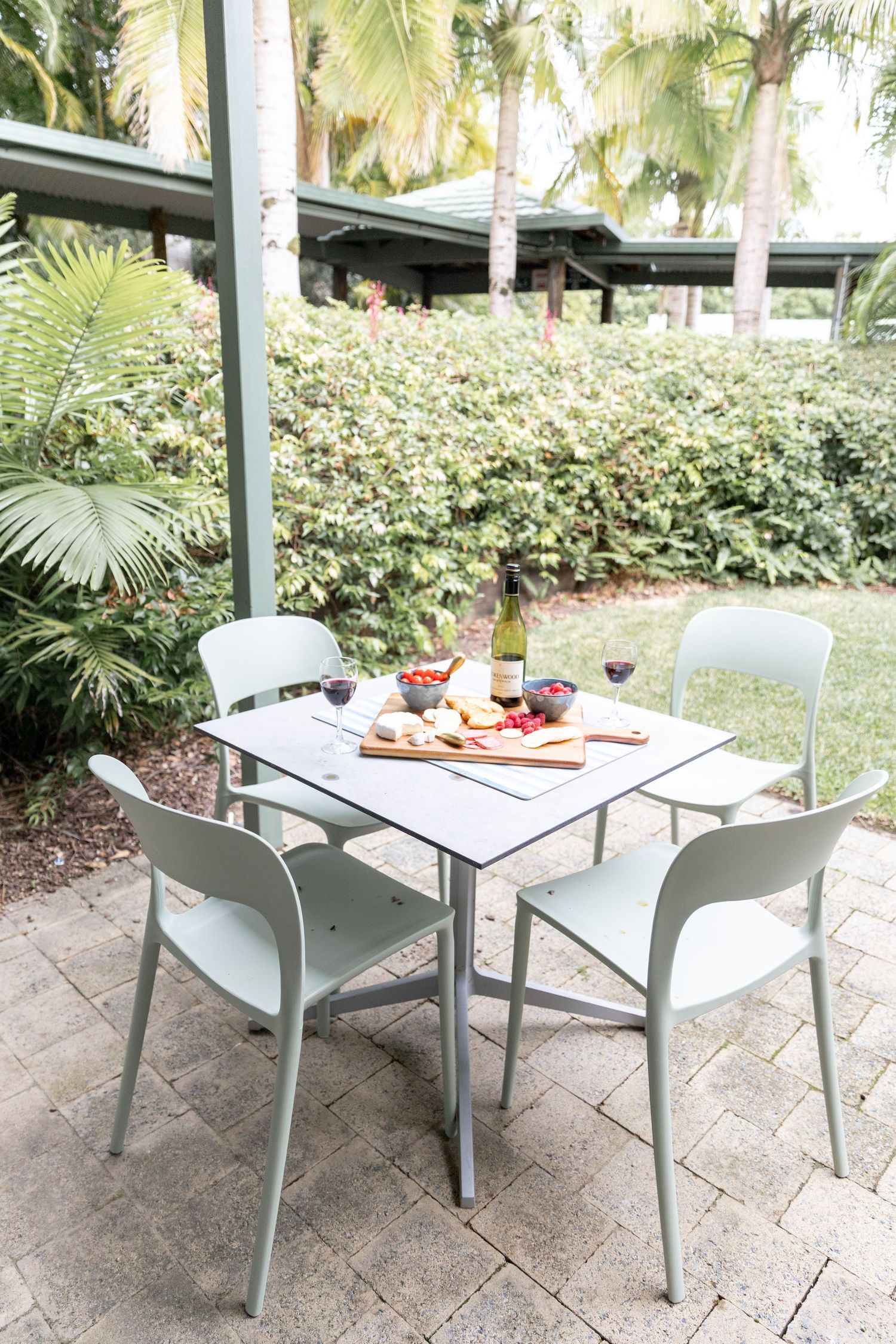 Outdoor patio dining area with modern white furniture set against tropical garden backdrop.