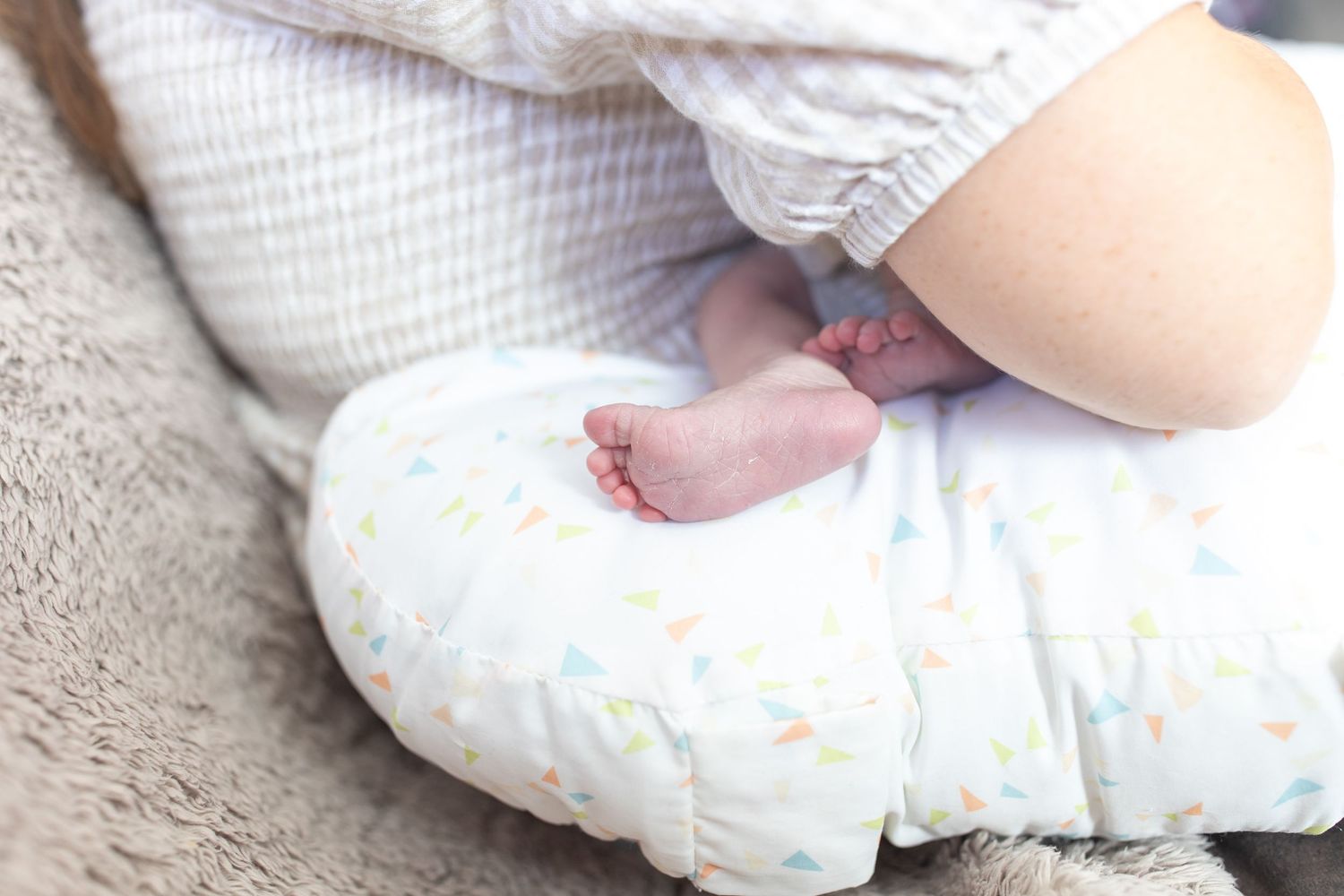 Close-up of a newborn baby's tiny feet resting on a white nursing pillow with colorful print.